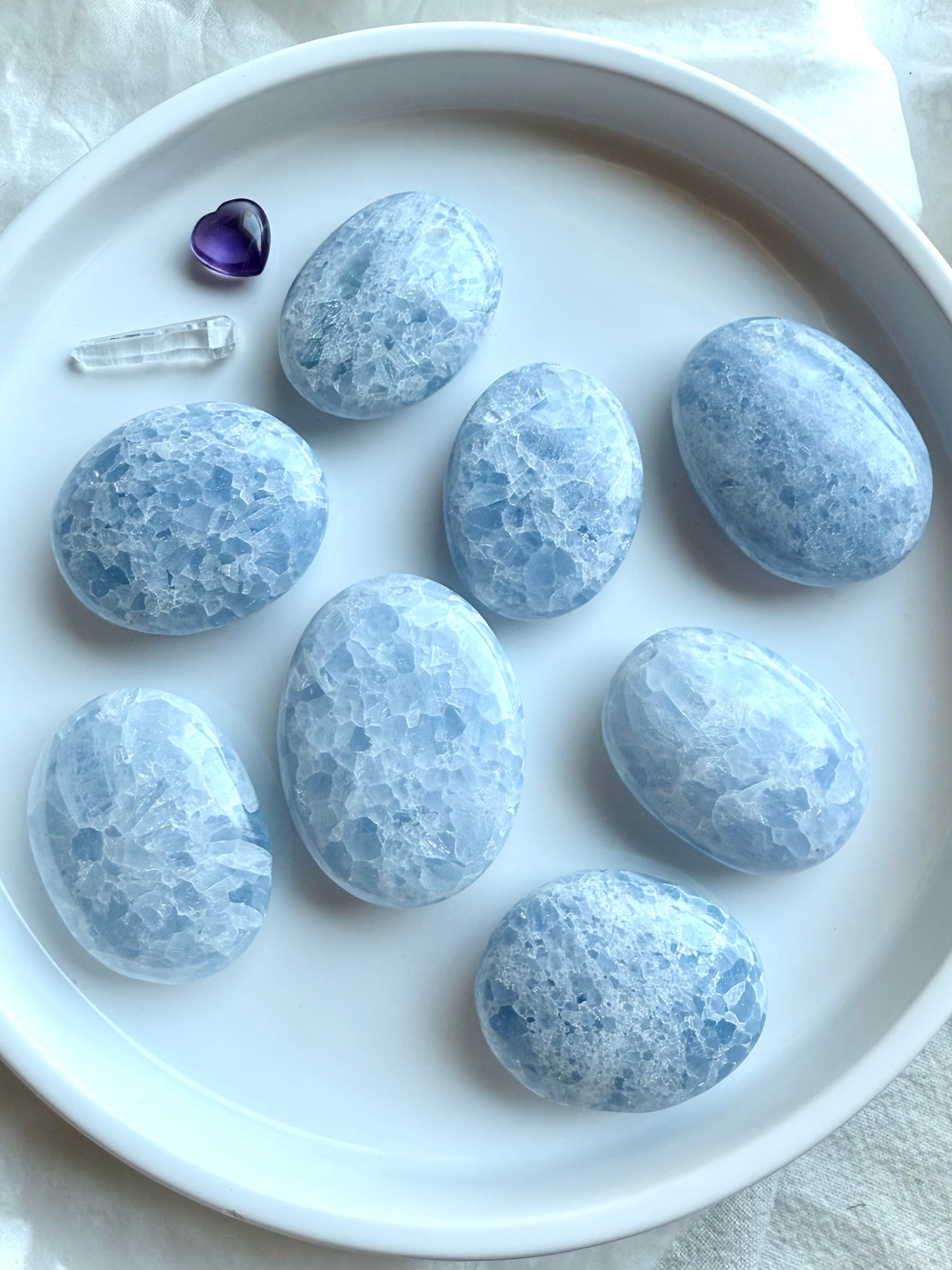 Flatlay of Blue Calcite palm stones on a white plate — polished healing crystals in irregular oval shapes with soft blue and white marbling