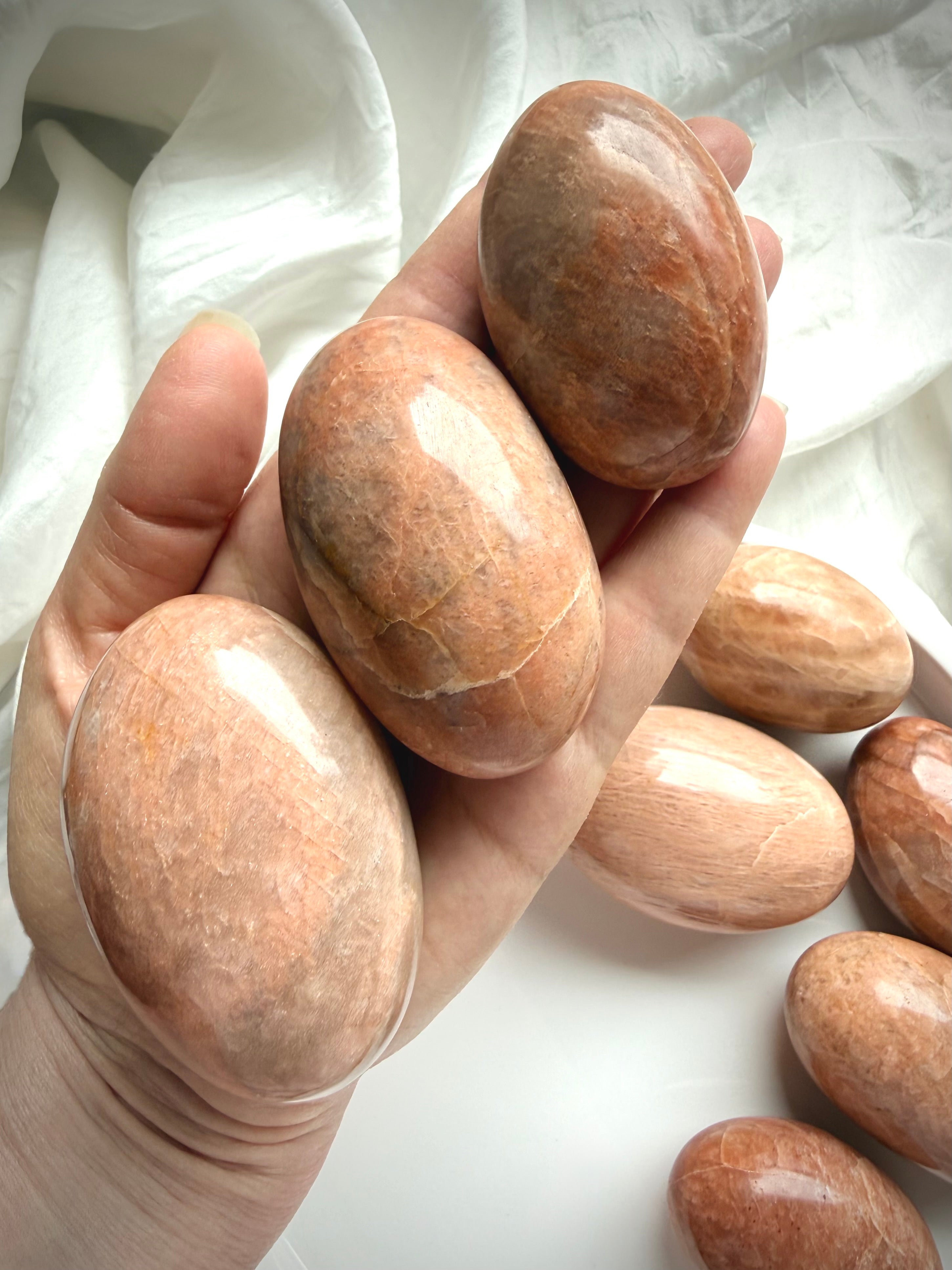 Hand holding large Peach Moonstone palm stones with warm peach tones, polished finish, and natural shimmer for meditation and emotional healing