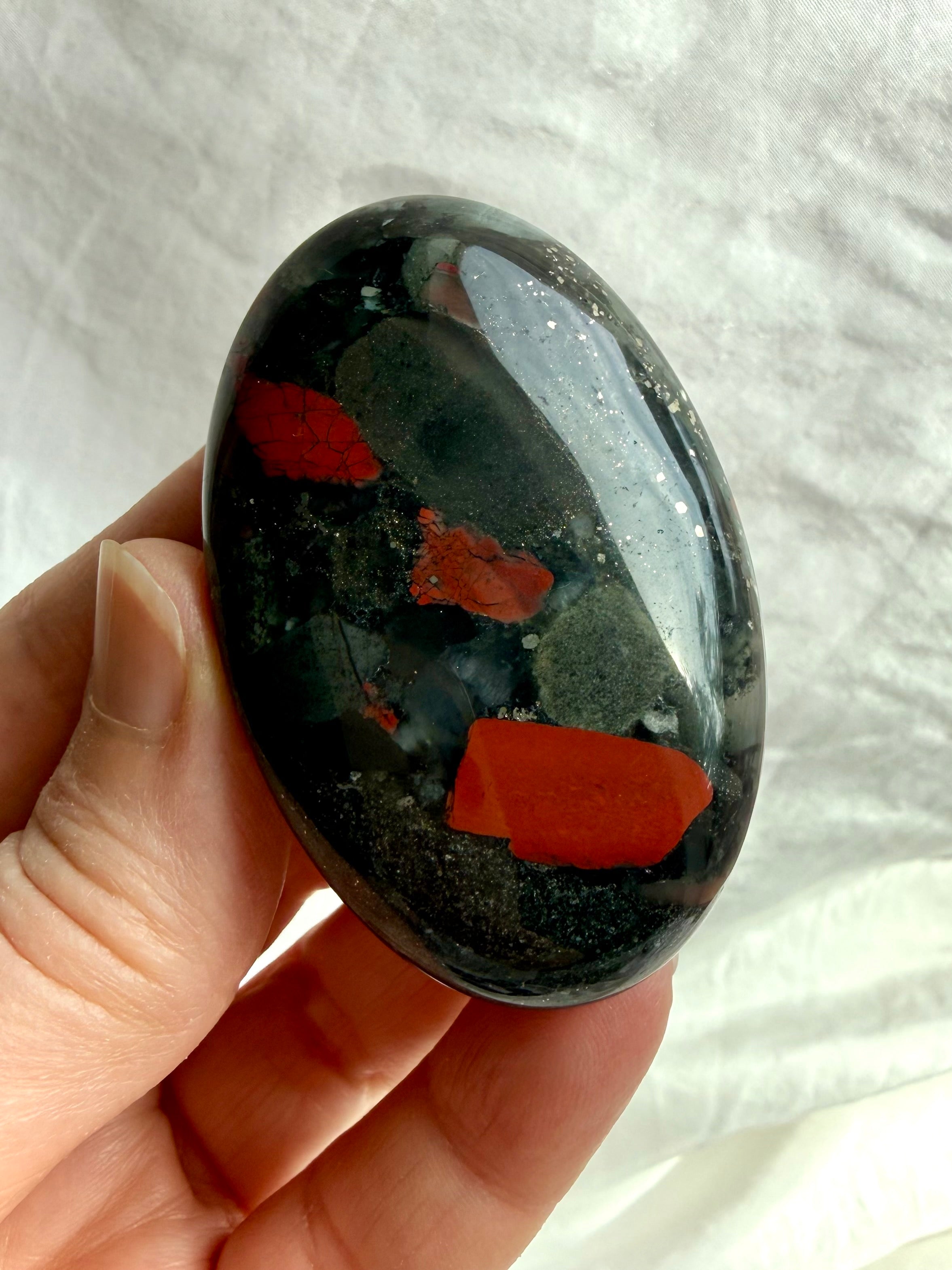 Bloodstone palm stone held in hand showing bold red inclusions, deep green tones and natural mineral patterning