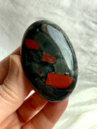 Bloodstone palm stone held in hand showing bold red inclusions, deep green tones and natural mineral patterning