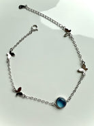 Delicate sterling silver bracelet with aquamarine crystal and butterfly charms shown on a white plate for high-vibe jewelry gifting