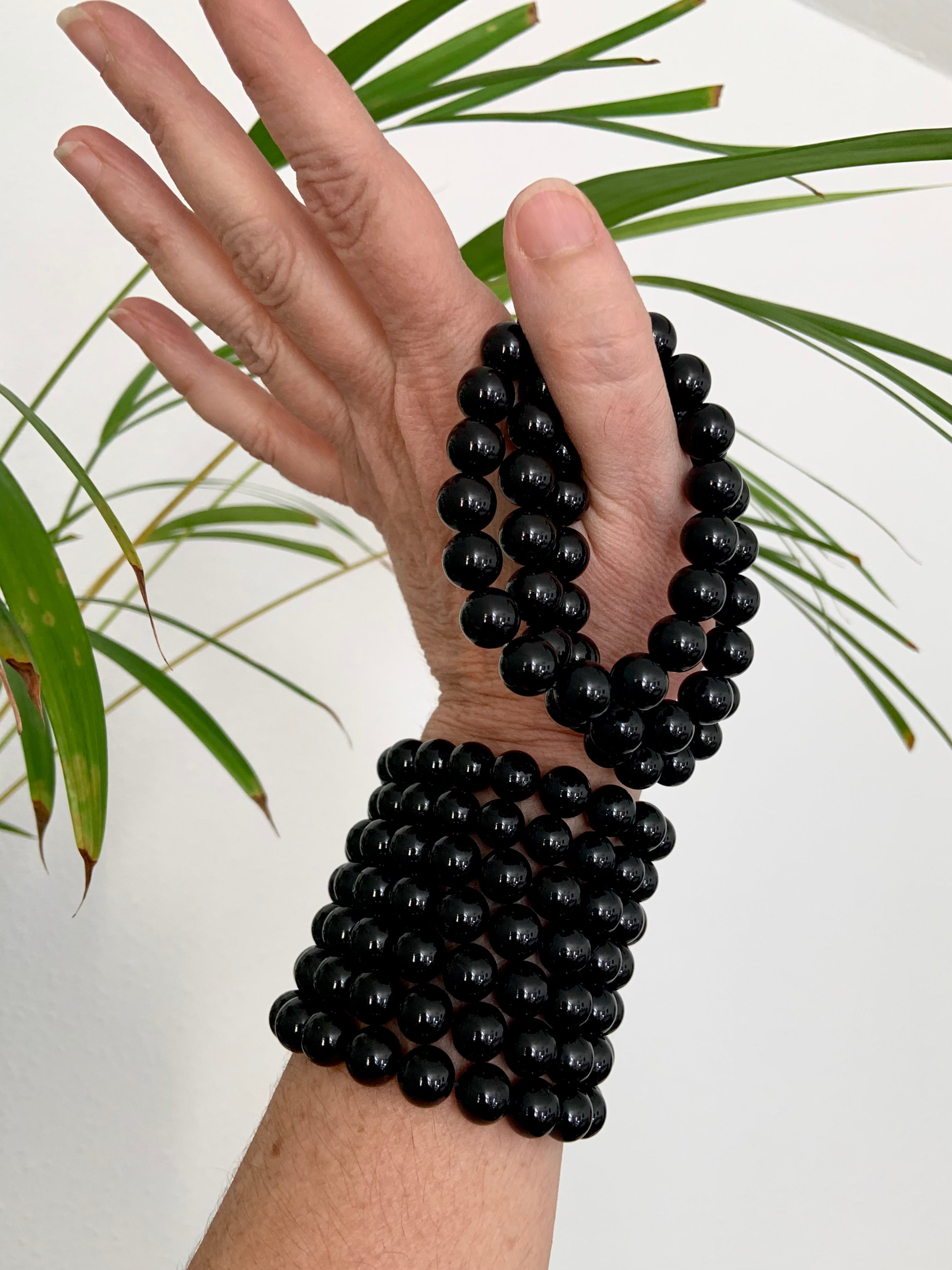 Stack of Black Tourmaline bracelets on wrist and held in hand with greenery in the background — natural setting for protective crystal jewelry