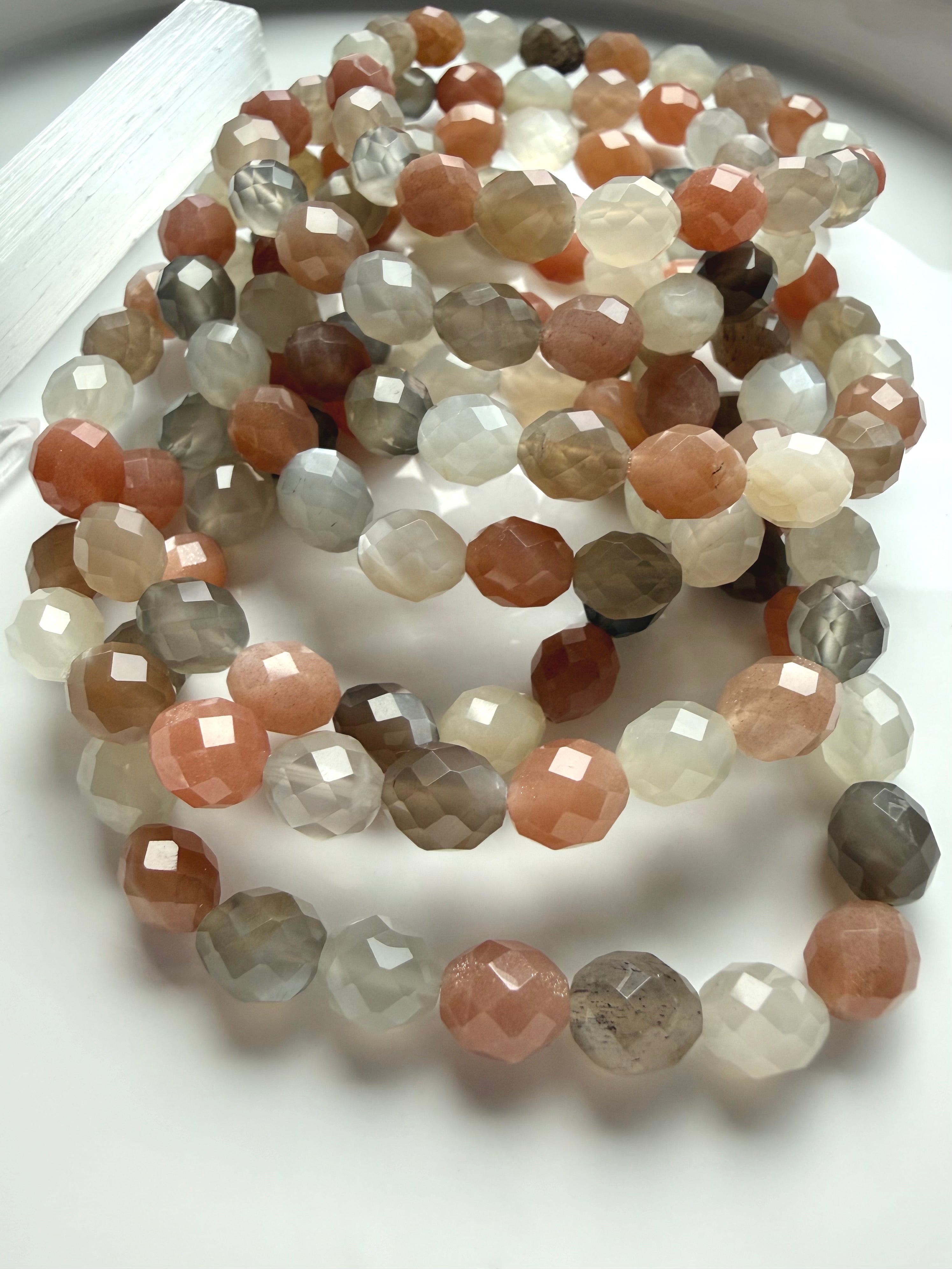 Faceted Moonstone crystal bracelets with peach, silver gray, and creamy white gemstones arranged in a luminous multicolor display