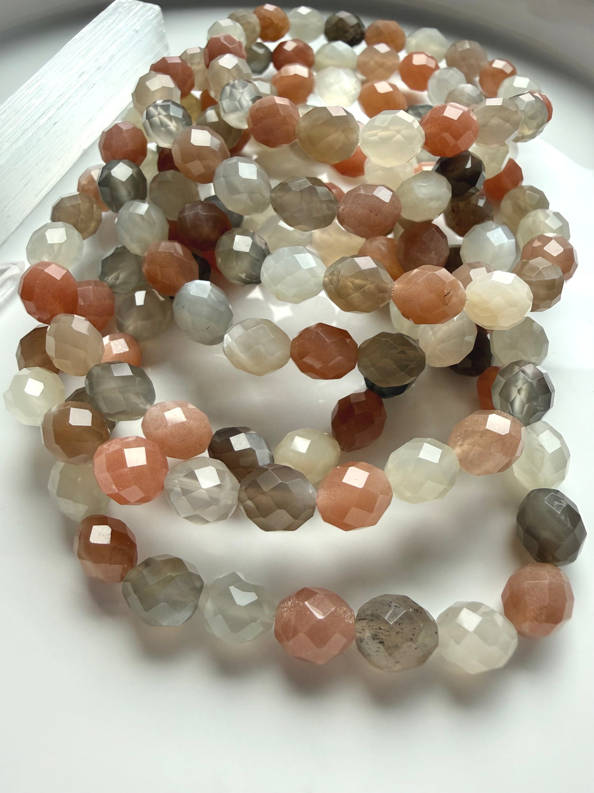 Faceted Moonstone crystal bracelets with peach, silver gray, and creamy white gemstones arranged in a luminous multicolor display