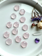 Wide view of array of mini rose quartz hexagon crystals on a white plate styled with roses, clear quartz point & amethyst heart for altar décor