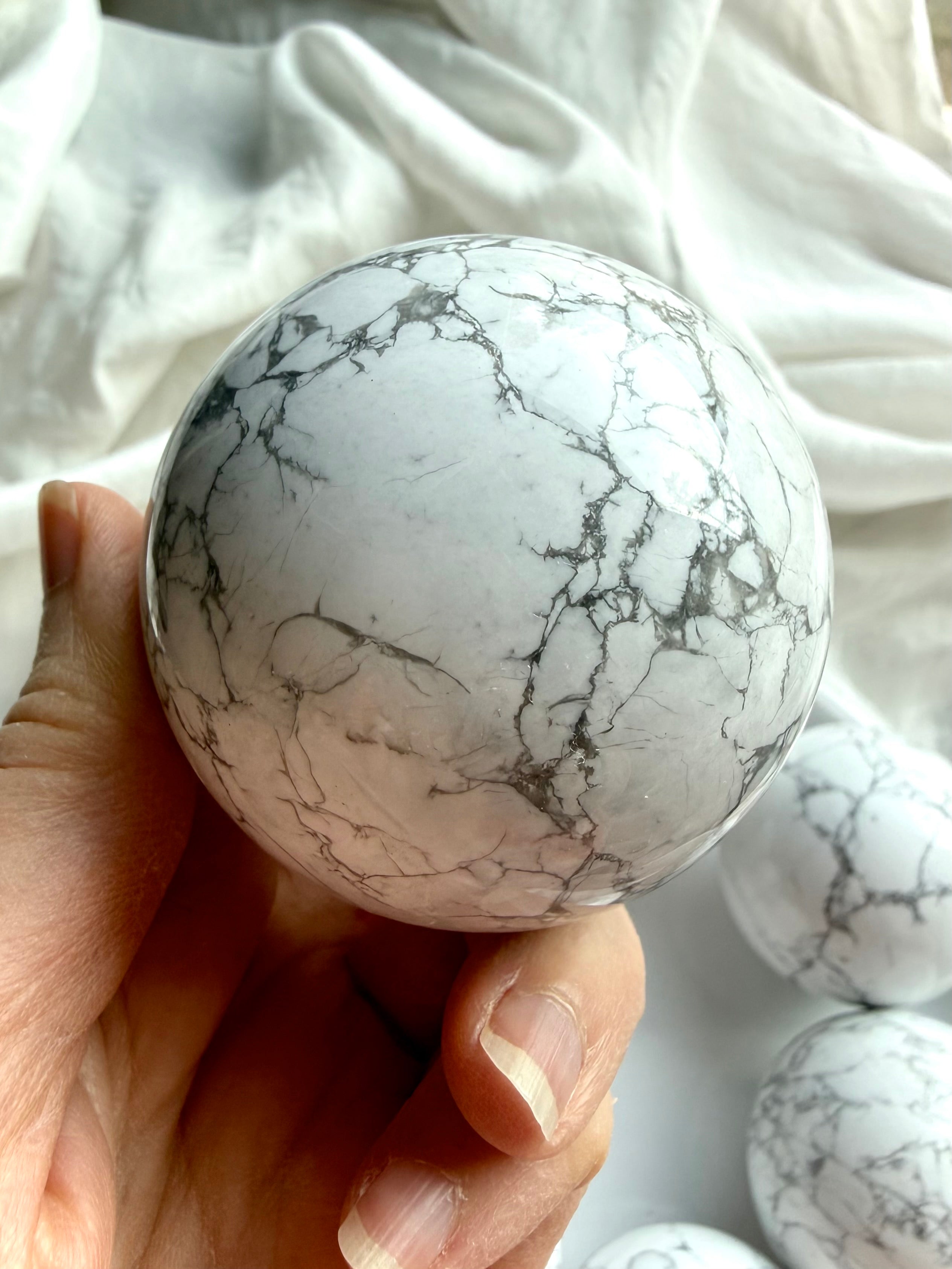 Close-up of Howlite crystal sphere in hand showing detailed gray veining on polished white stone, calming crystal for stress relief and peaceful energy