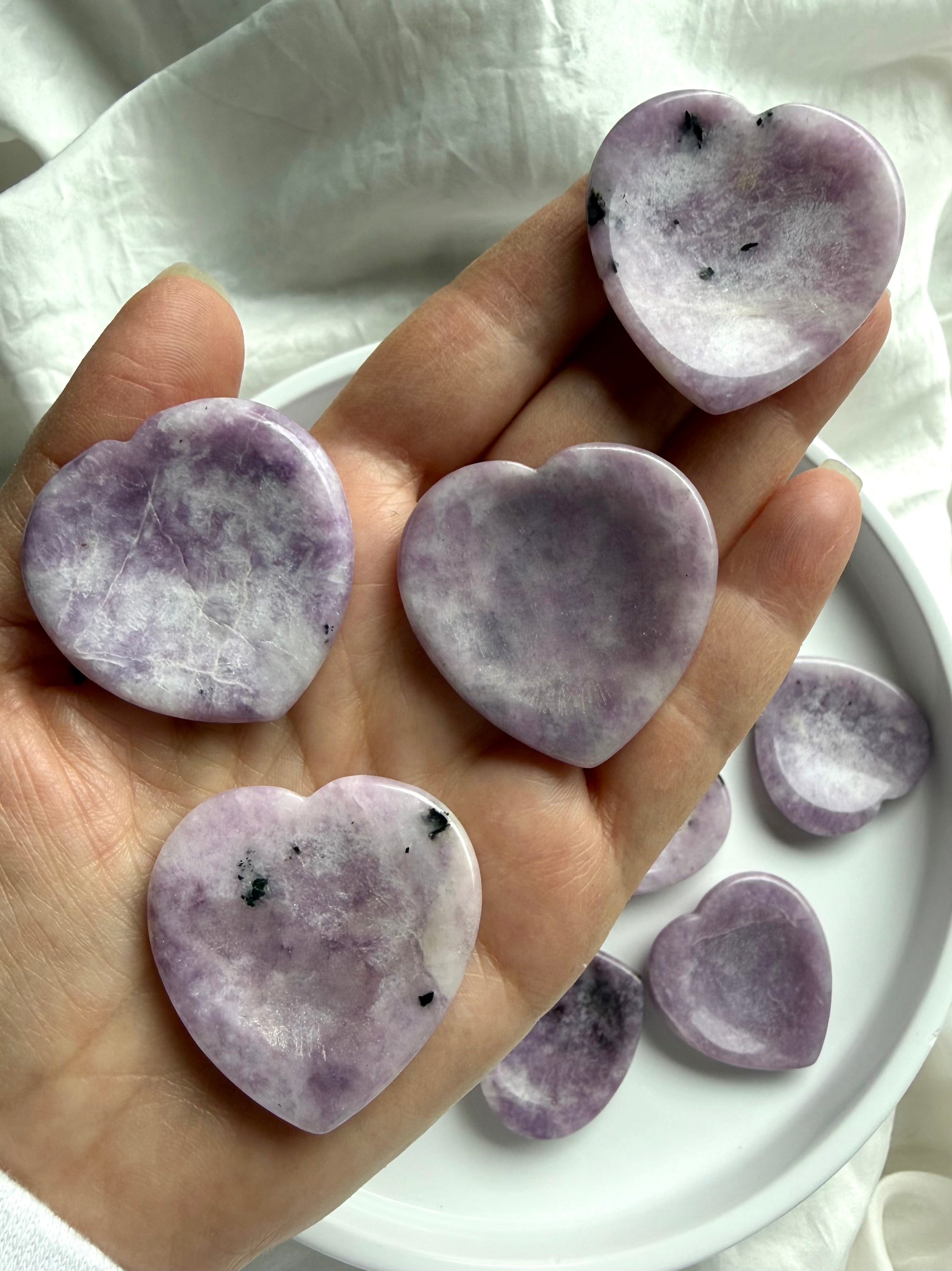 Lepidolite heart worry stones in hand showing mottled lilac purple color with white and gray inclusions