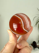 A banded carnelian crystal ball with an intricate chevron pattern swirling around the sphere