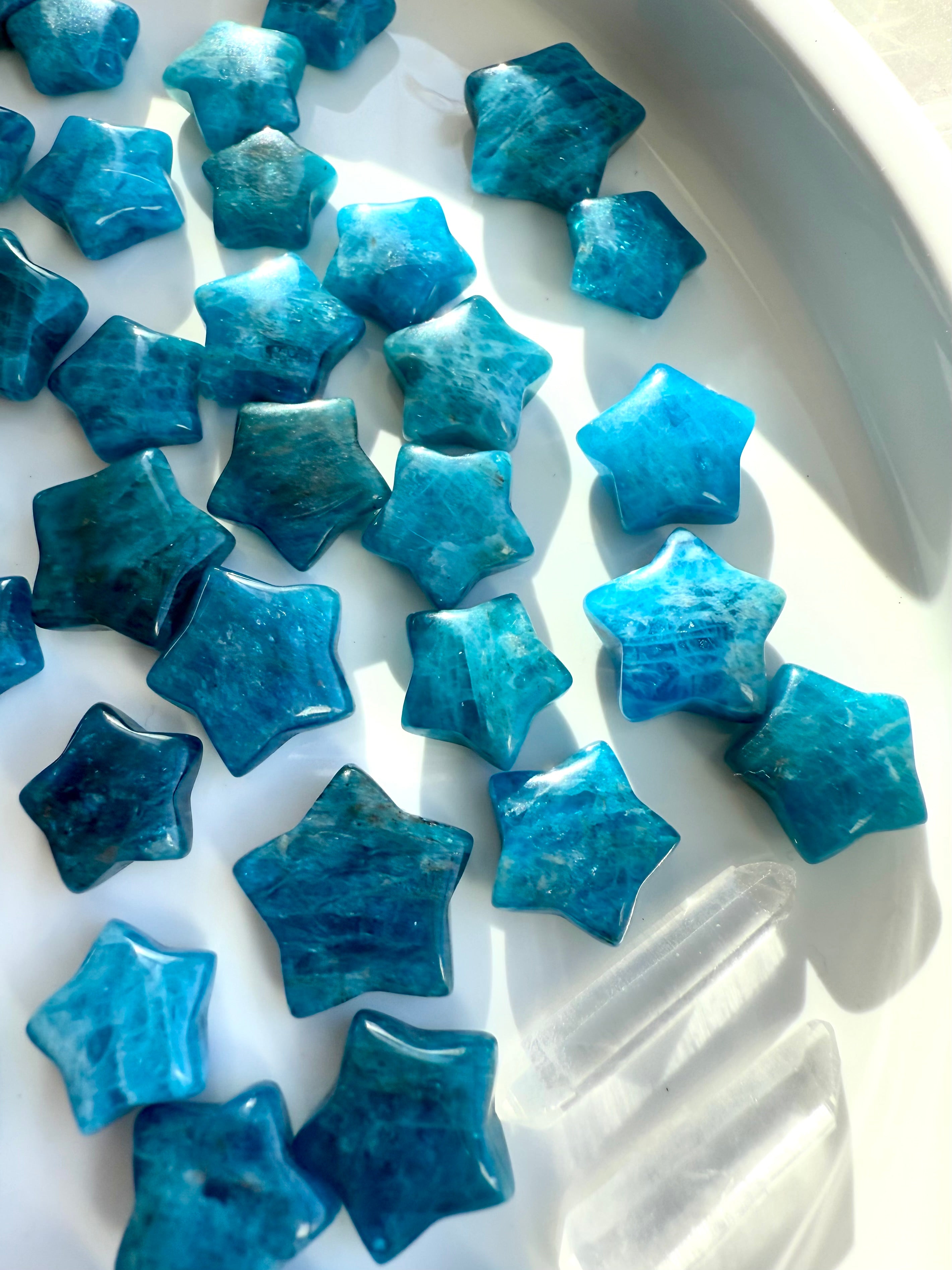 Close-up of Blue Apatite mini stars on white plate with clear quartz point — vibrant teal crystal stars for inspiration & energetic flow.