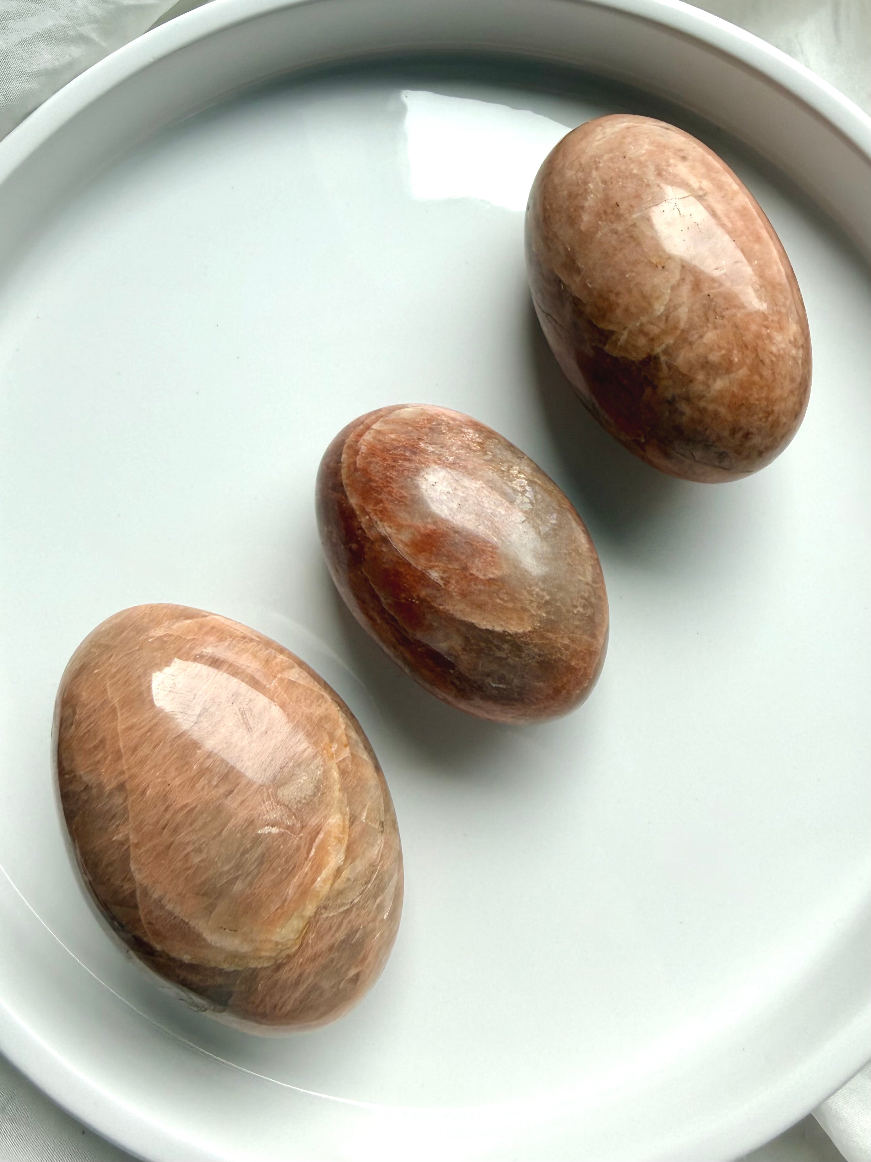 Three polished Peach Moonstone palm stones with rounded grounding shapes and warm feminine energy tones