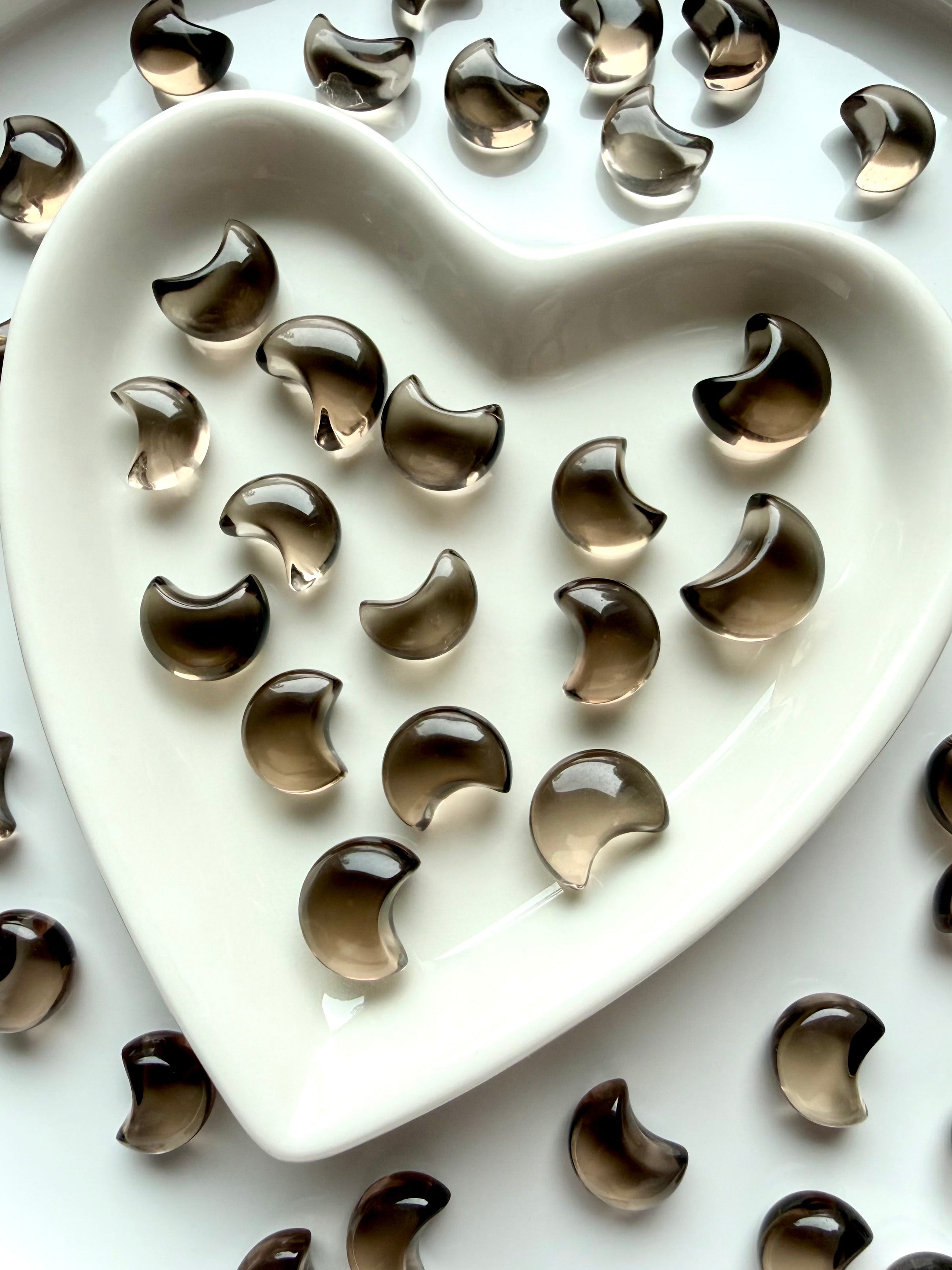 Tiny Smoky Quartz crescent moons displayed in a heart-shaped crystal dish with polished translucent brown crystal carvings