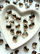 Tiny Smoky Quartz crescent moons displayed in a heart-shaped crystal dish with polished translucent brown crystal carvings