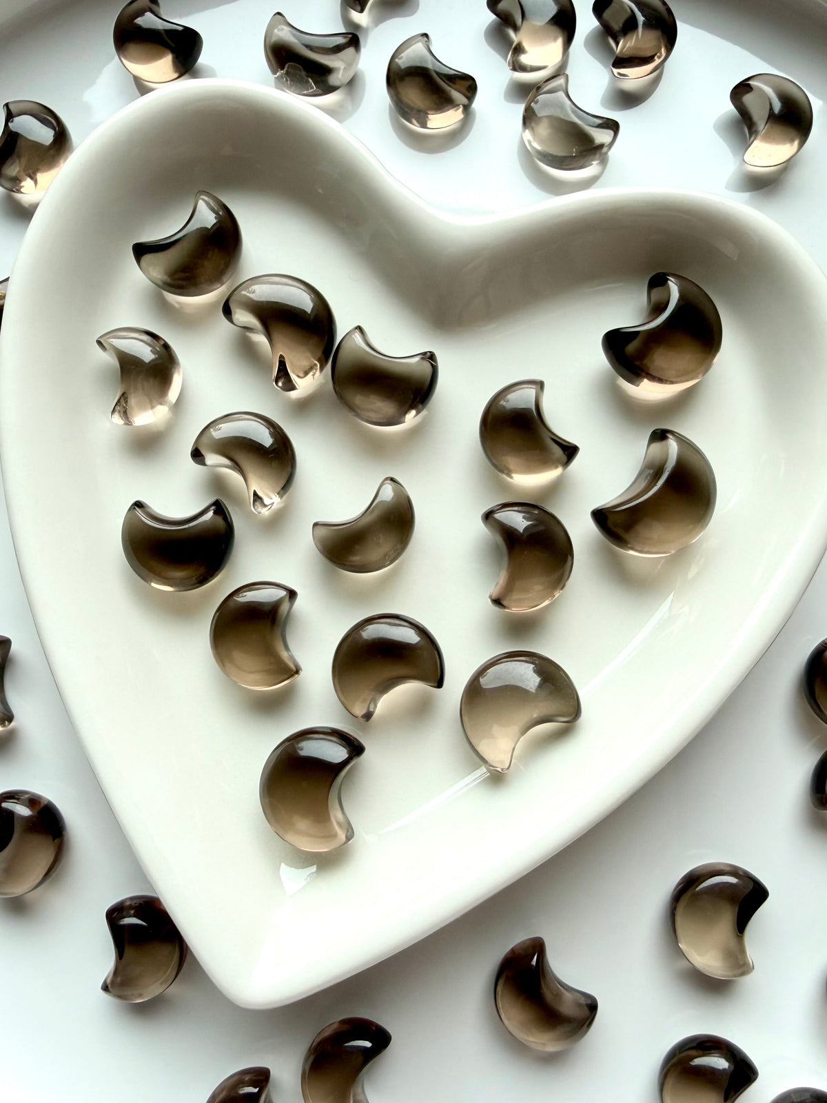 Tiny Smoky Quartz crescent moons displayed in a heart-shaped crystal dish with polished translucent brown crystal carvings