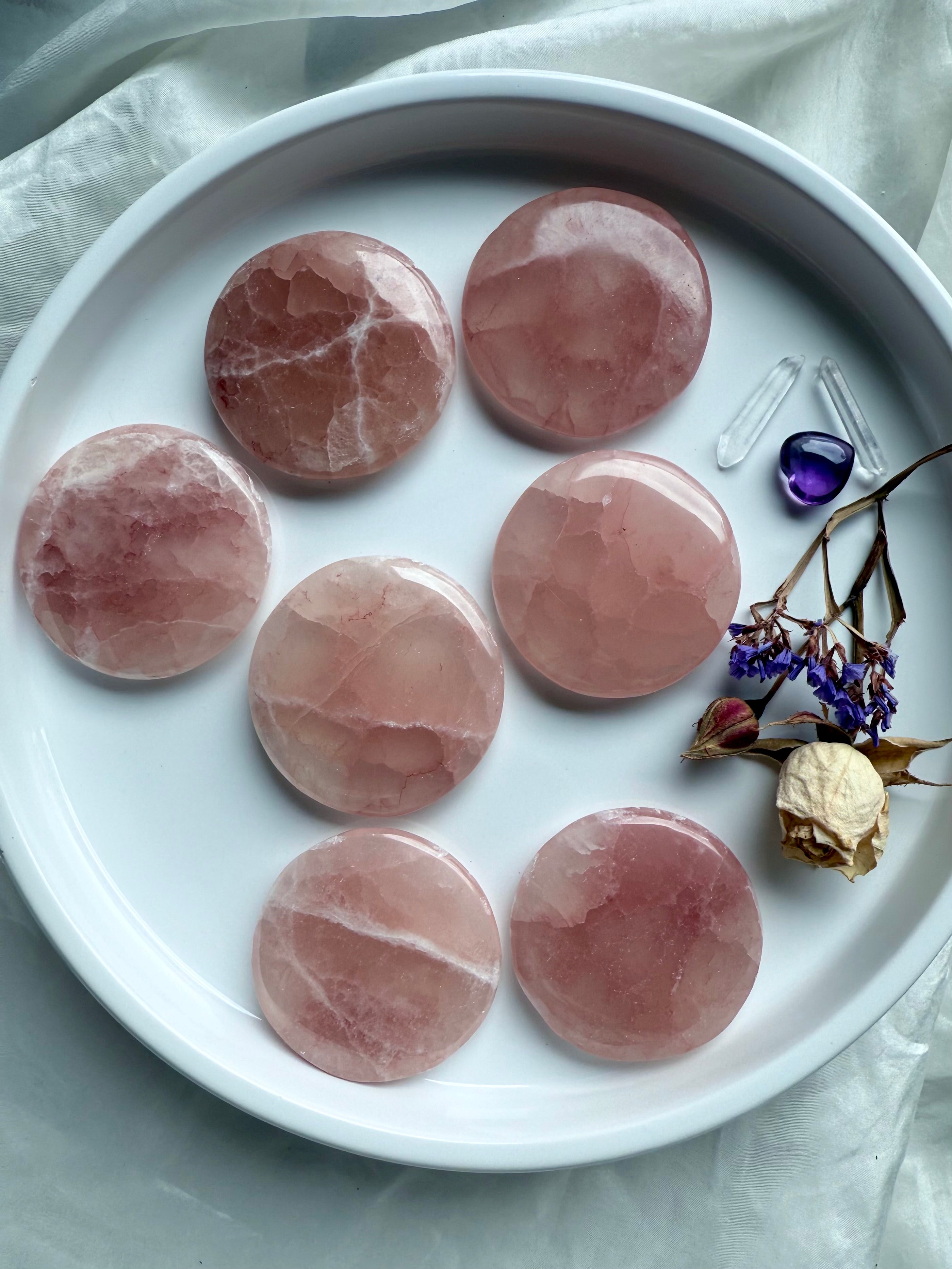 Rose Calcite meditation stones with soft pink patterns arranged in a white dish with dried flowers and mini crystals
