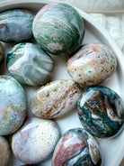 Ocean Jasper crystal palm stones in a white bowl, displaying colorful agate banding, orbicular patterns, and natural variation