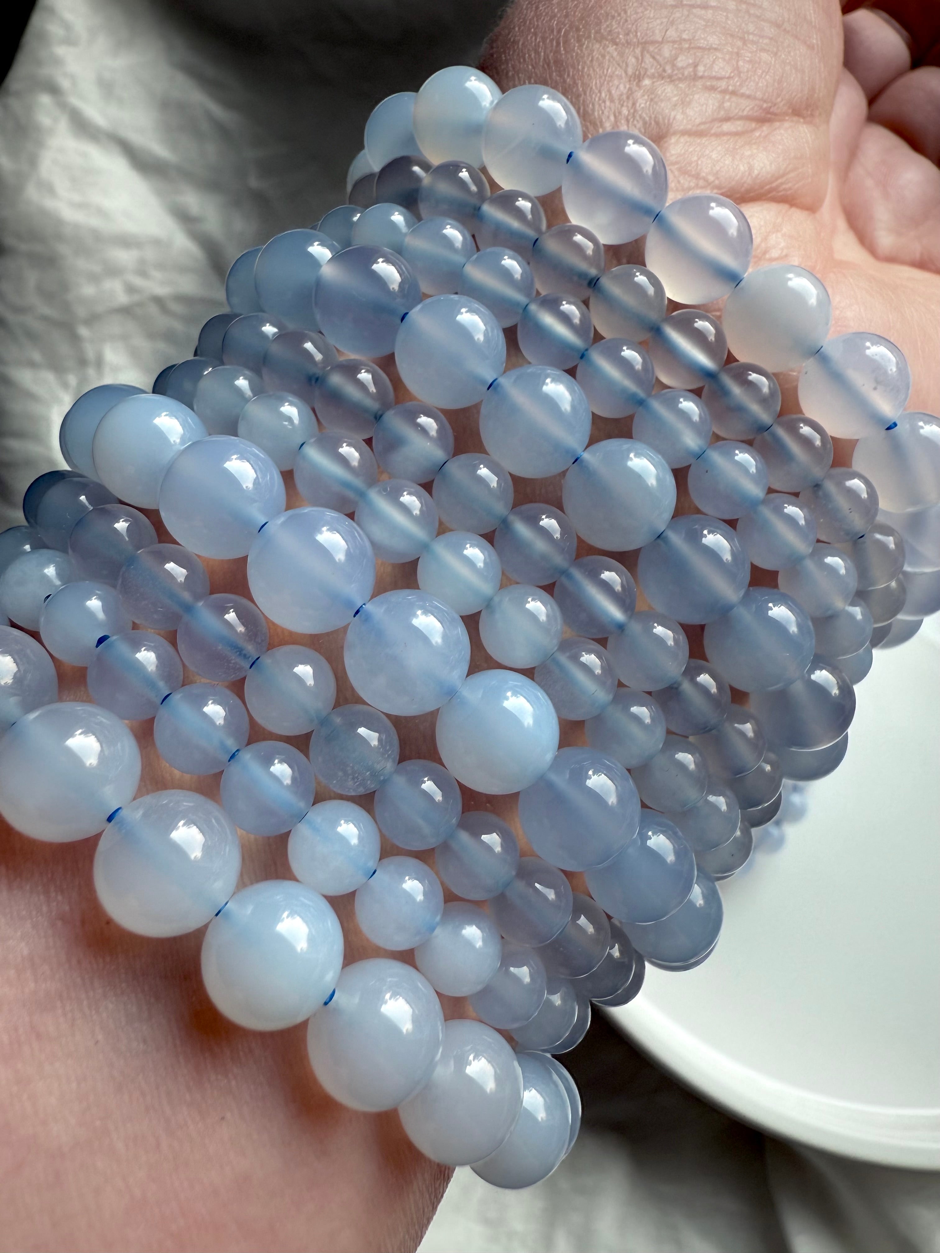 Glossy Blue Chalcedony bead bracelets in varied sizes layered on wrist — high-quality throat chakra crystal jewelry for peace