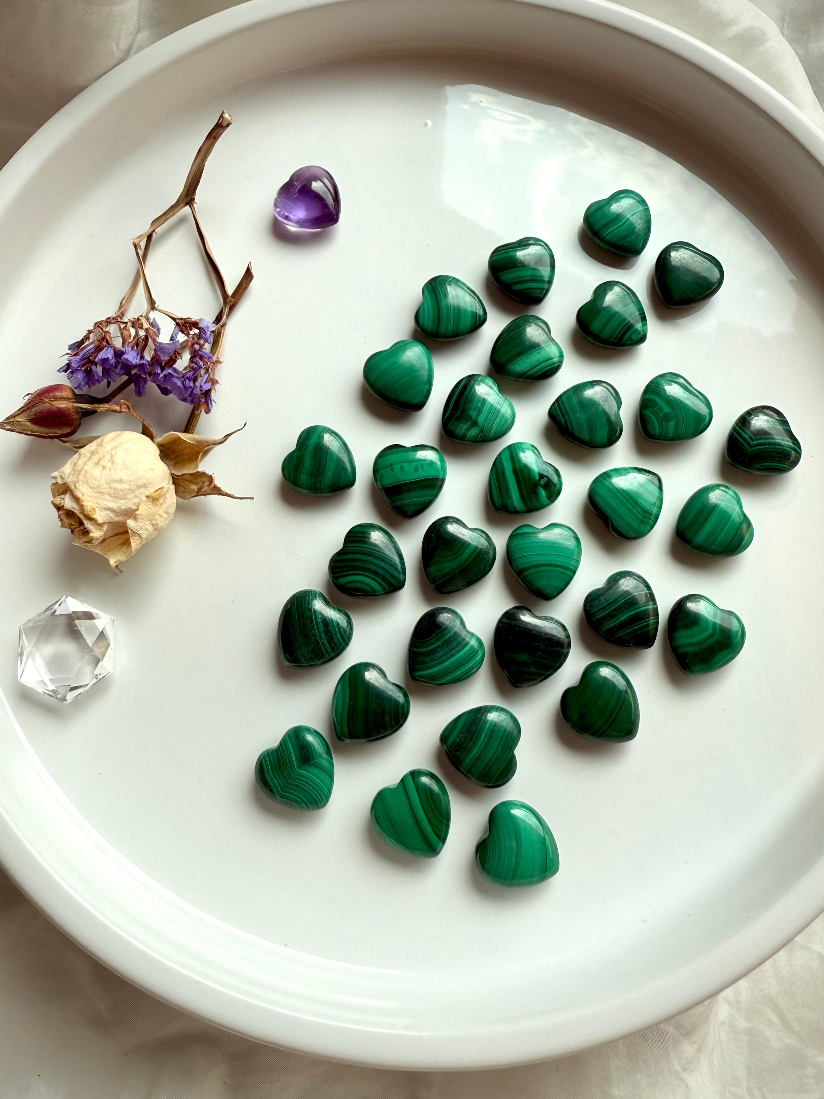 Mini Malachite crystal hearts arranged on a white plate with dried flowers and quartz points for sacred altar styling