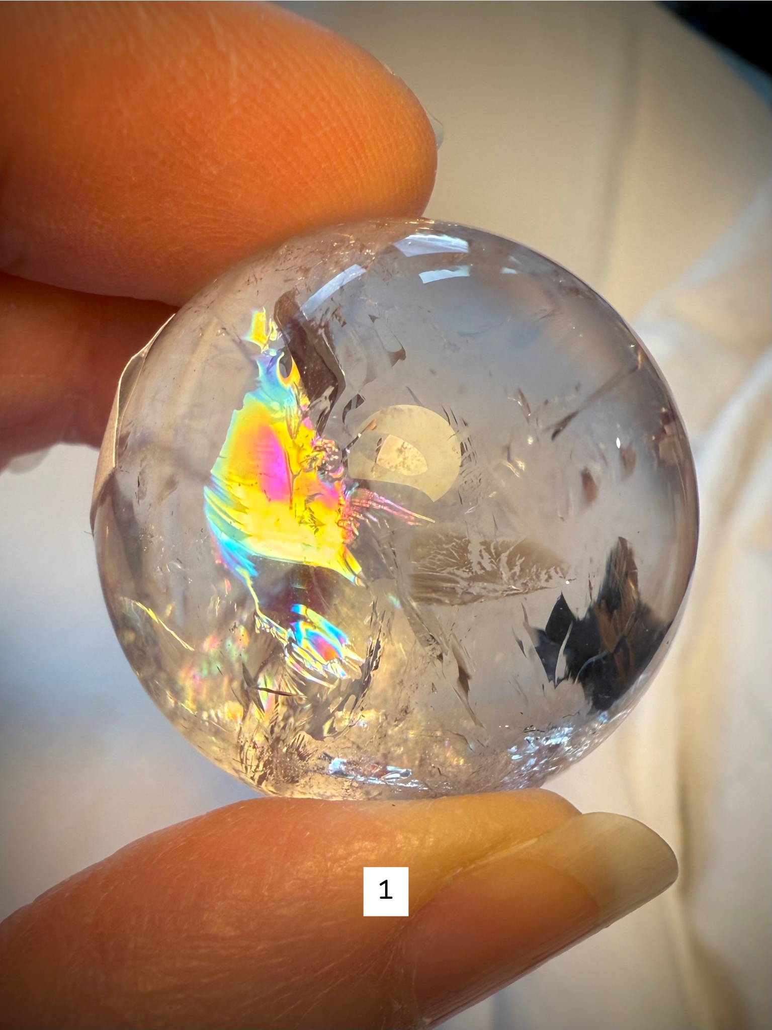 Close-up of Rainbow Quartz sphere #1 showing a vivid rainbow inclusion and clear crystalline structure.