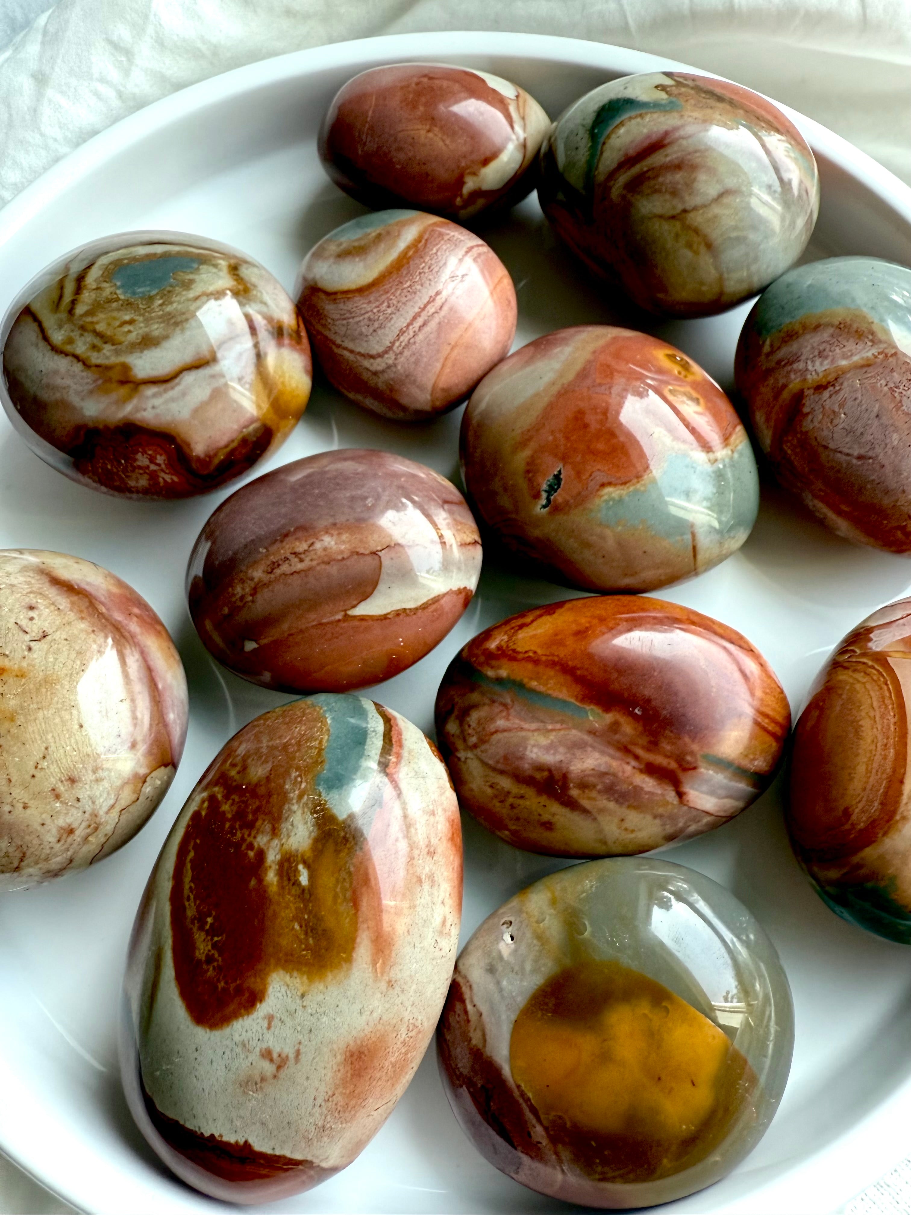 Polychrome Jasper palm stones on a white plate, showing earthy tones & swirled patterns for grounding energy