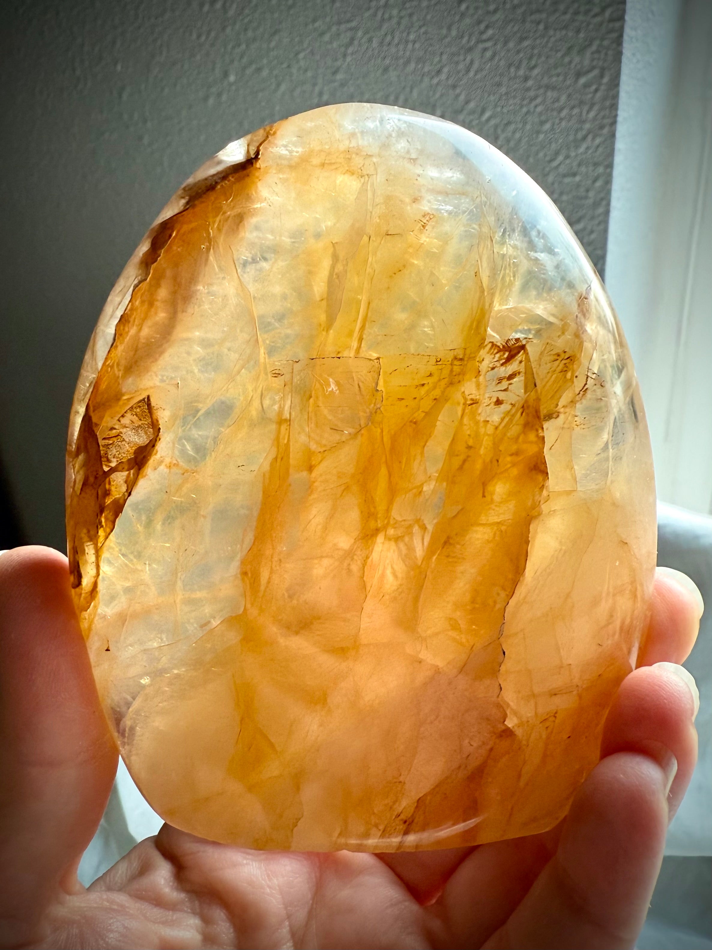 Golden Healer Quartz crystal sculpture held to the light showing translucent golden tones