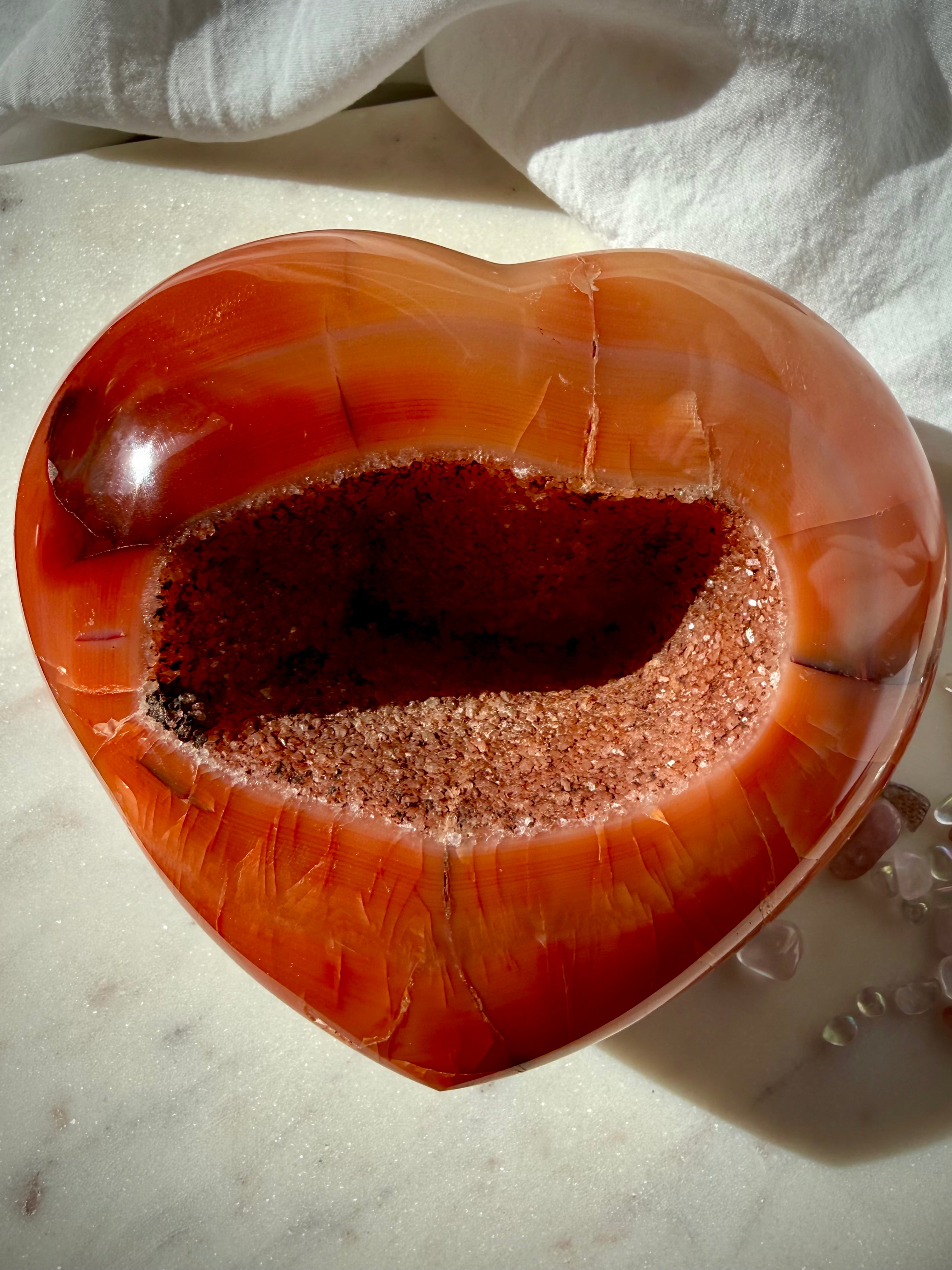 One of a kind Carnelian geode heart held in hand showcasing glittering druzy center and natural red-orange patterns