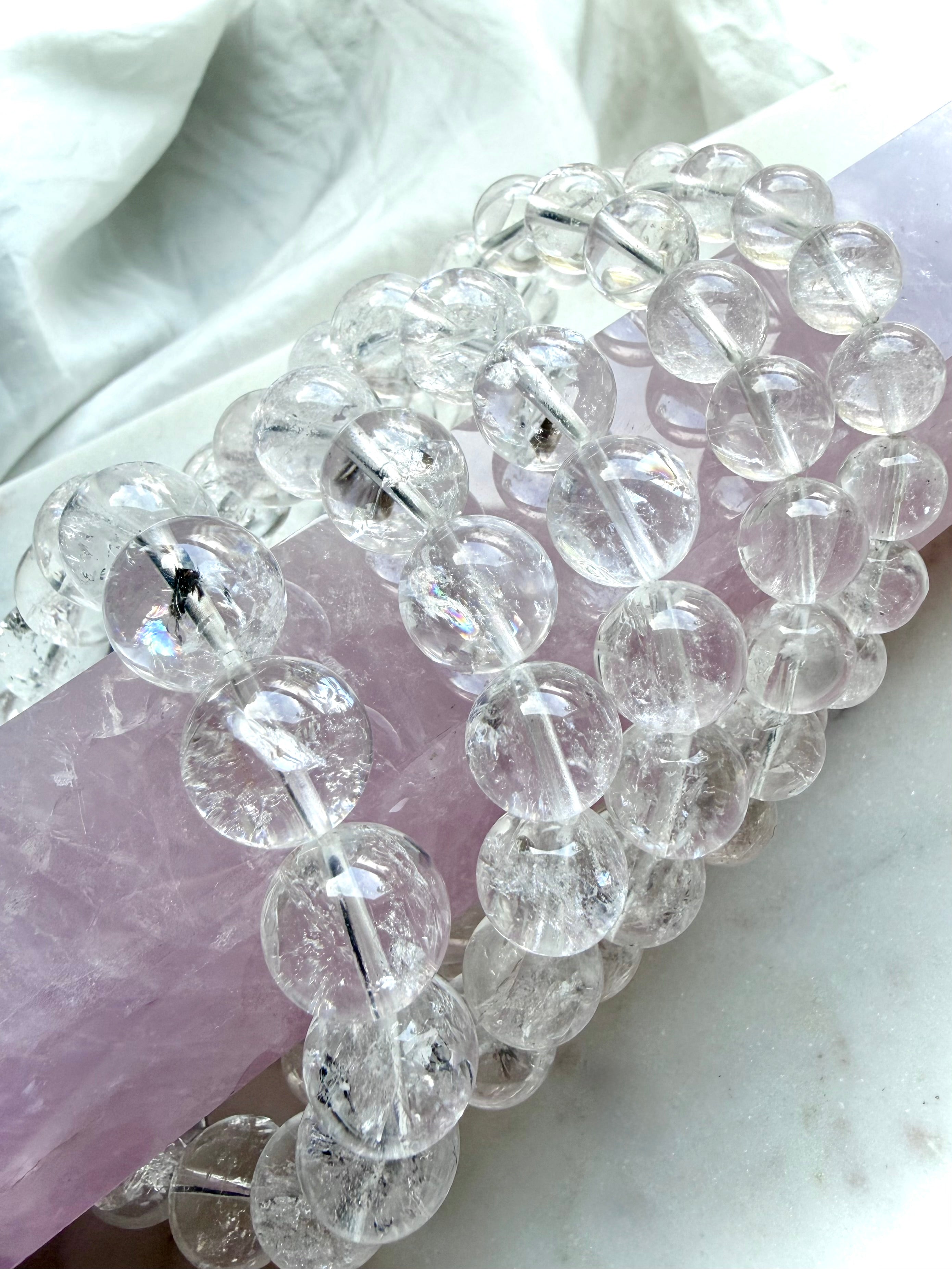 Rainbow Clear Quartz bracelet displayed on pink rose quartz with luminous transparent crystal beads