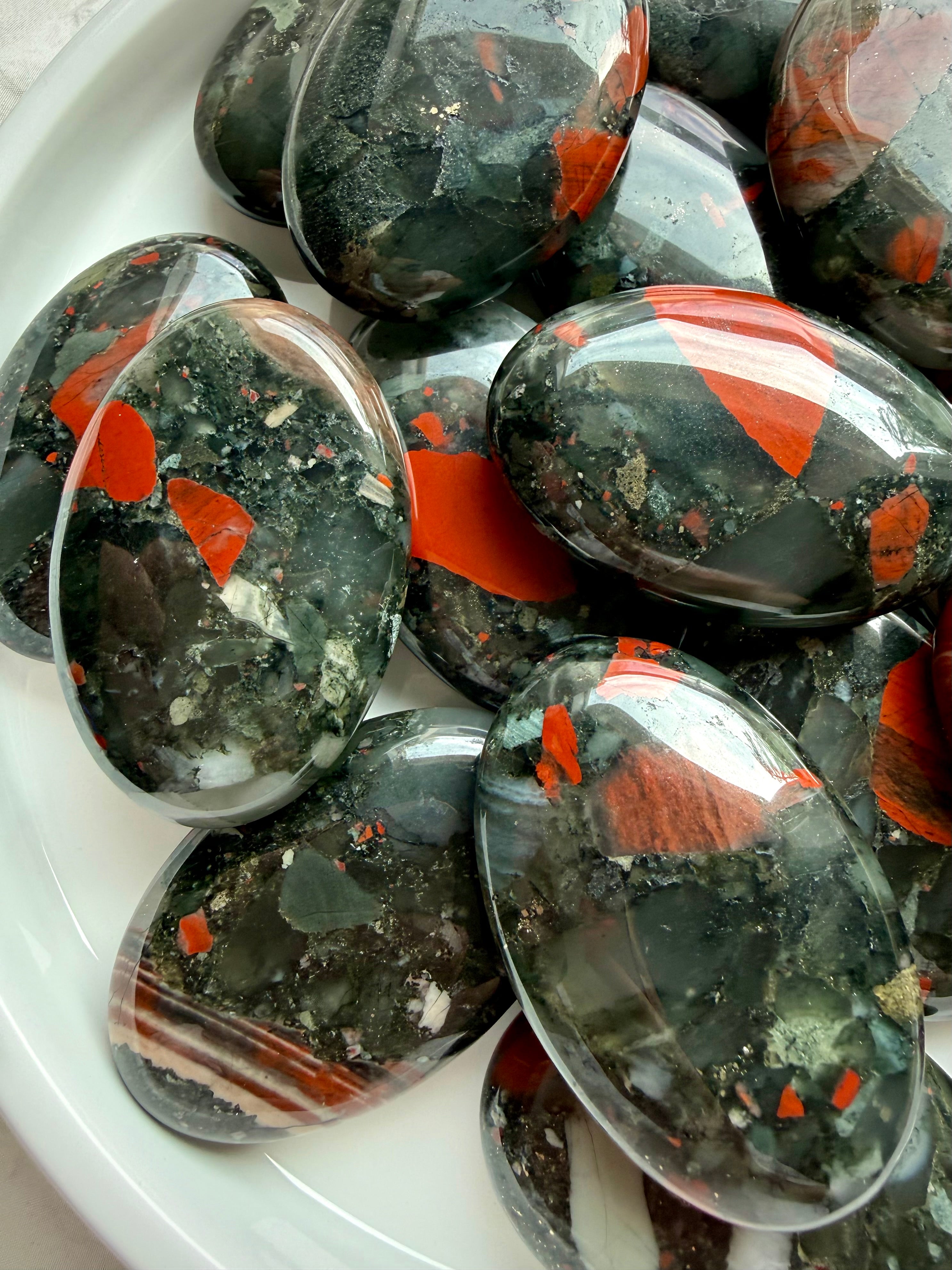 Natural Bloodstone palm stones showing varied red and green patterns, mineral inclusions and glossy polished surfaces