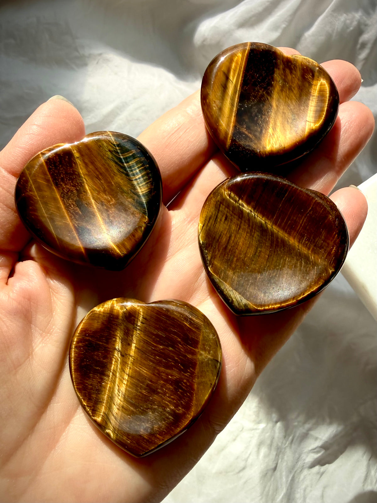 Four Tiger’s Eye heart worry stones held in hand, showcasing golden chatoyancy, rich brown tones, and unique natural patterns