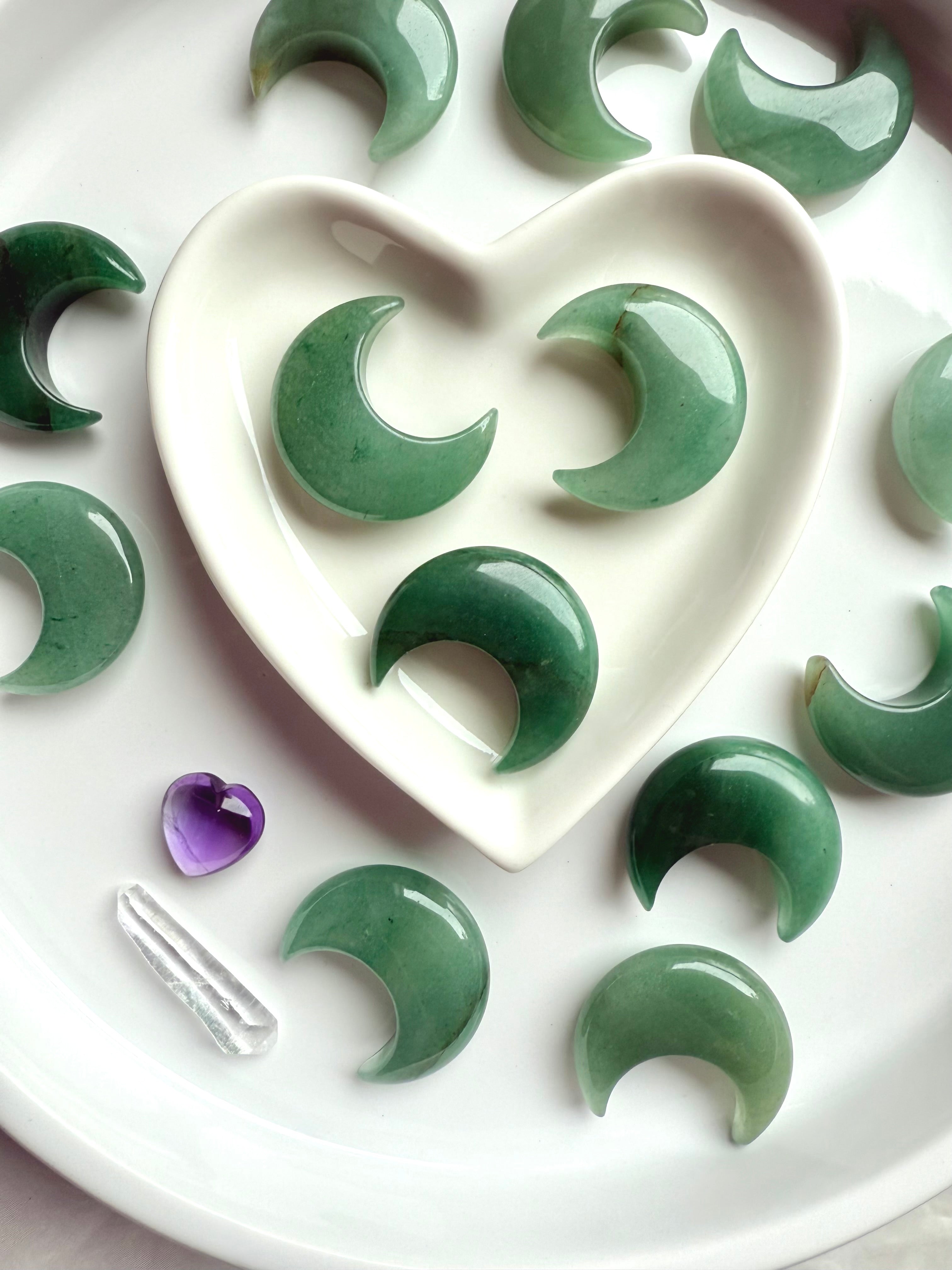 Closeup of Green Aventurine crescent moons in a white heart bowl surrounded by more moons, soothing crystals for love and abundance