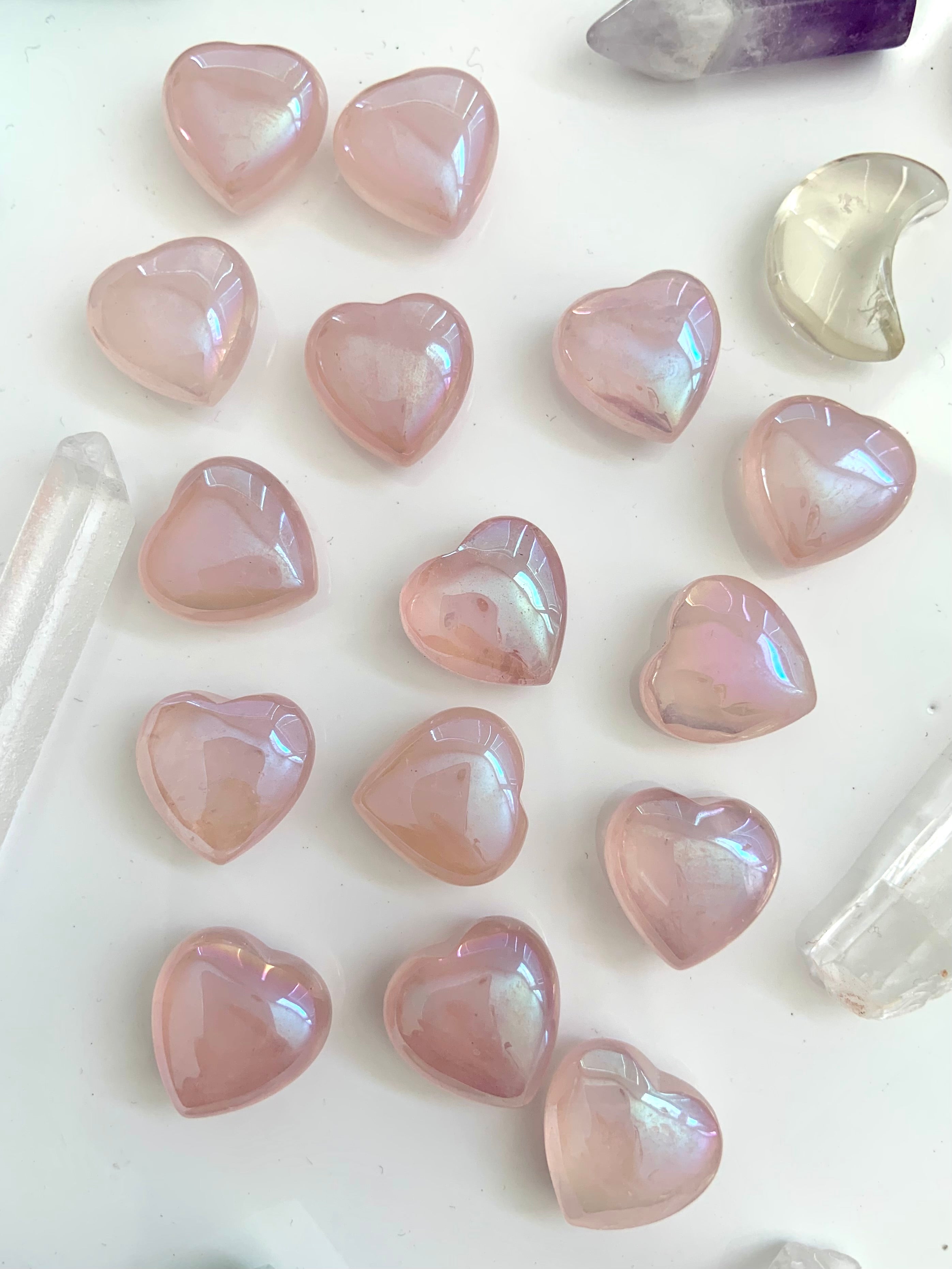 Flatlay of iridescent rose quartz aura hearts with other crystals on white — high-vibe pink crystals for love, peace, & spiritual connection