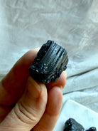 Natural Black Tourmaline crystal held in hand showing rough texture and deeply striated crystal growth