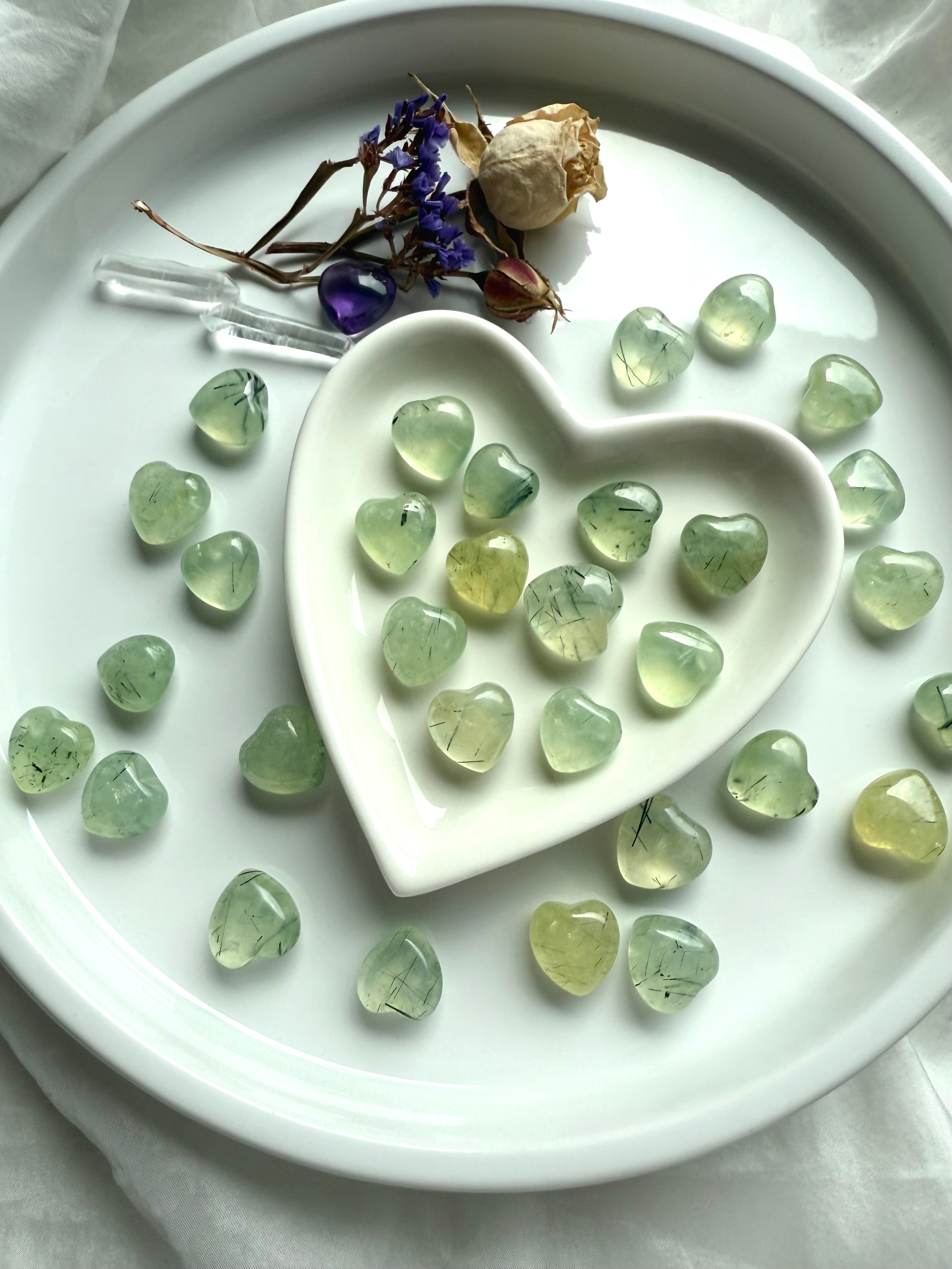 Mini Crystal Hearts made from Prehnite with Epidote polished for smooth texture, displayed on white ceramic plate and heart bowl.