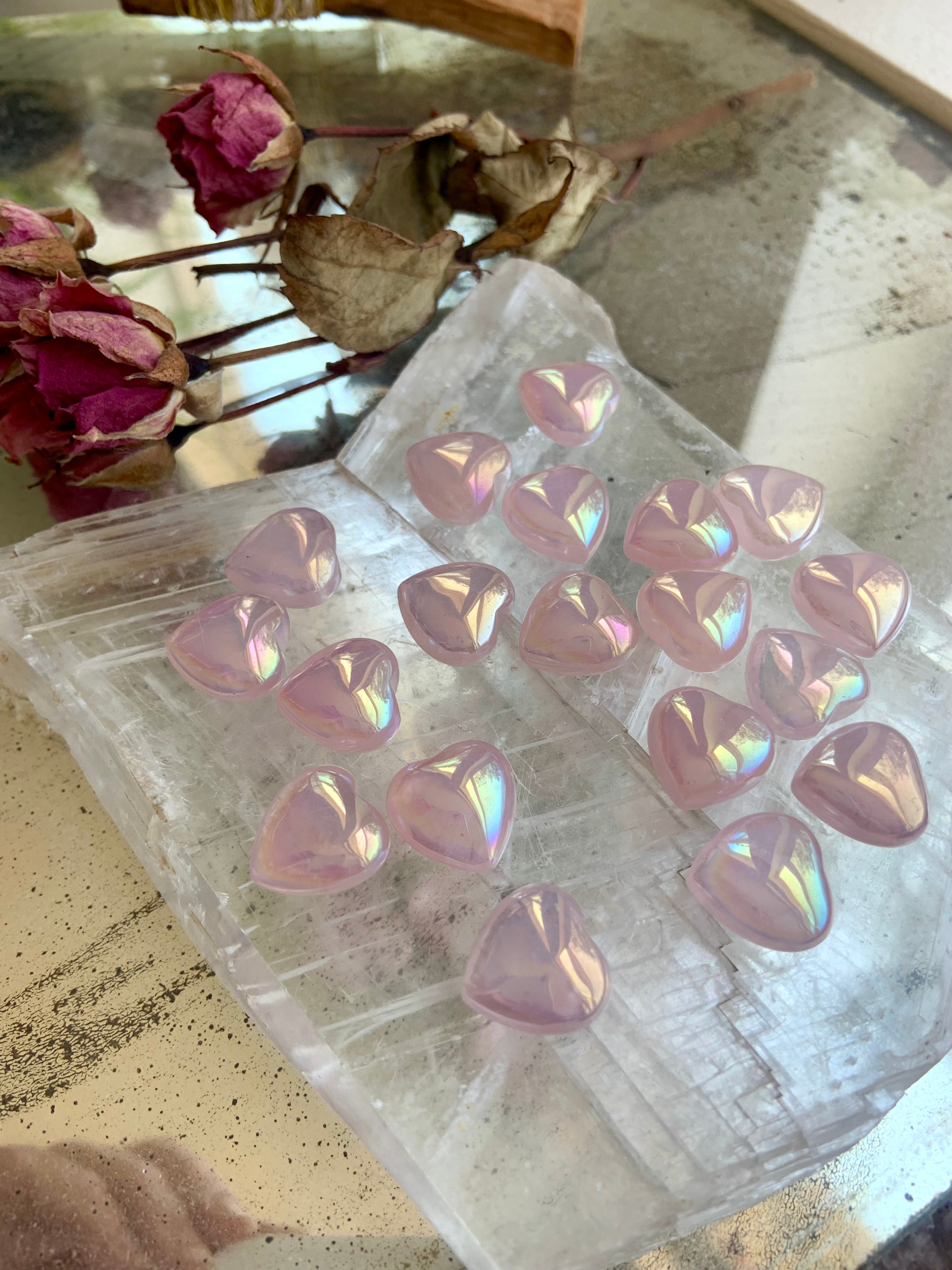 Close-up of aura rose quartz hearts on a mirrored selenite slab — iridescent pink stones reflecting light for love, beauty & emotional healing