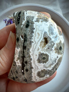 Ocean Jasper Crescent Moon palm stone with gray and black orbicular starburst patterns held in hand for grounding, strength and inner healing