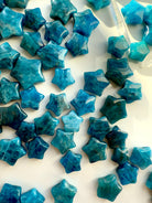 Overhead view of Blue Apatite mini crystal stars arranged on white silk — teal Throat Chakra stones for clarity, communication & inspiration.
