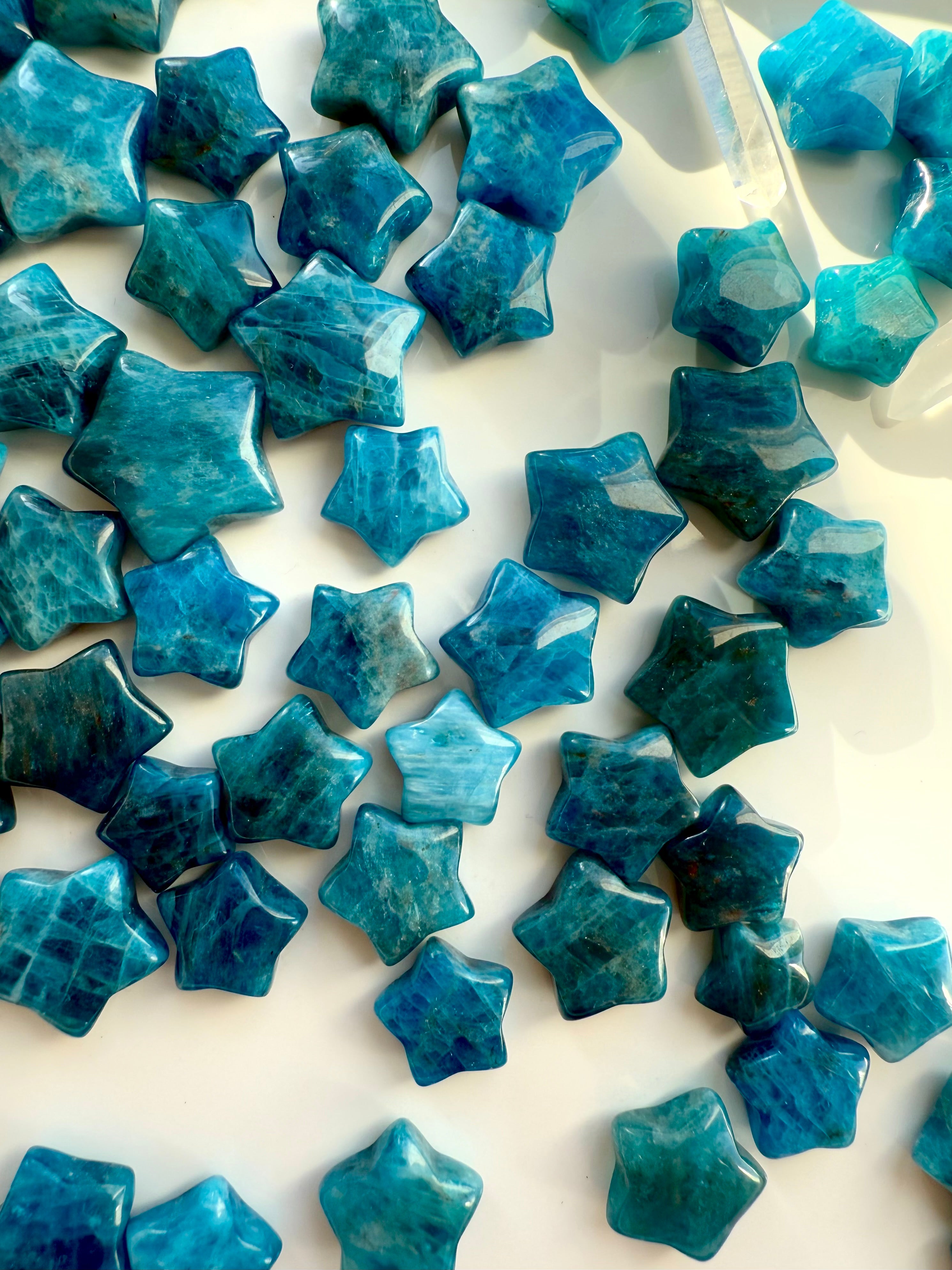 Overhead view of Blue Apatite mini crystal stars arranged on white silk — teal Throat Chakra stones for clarity, communication & inspiration.