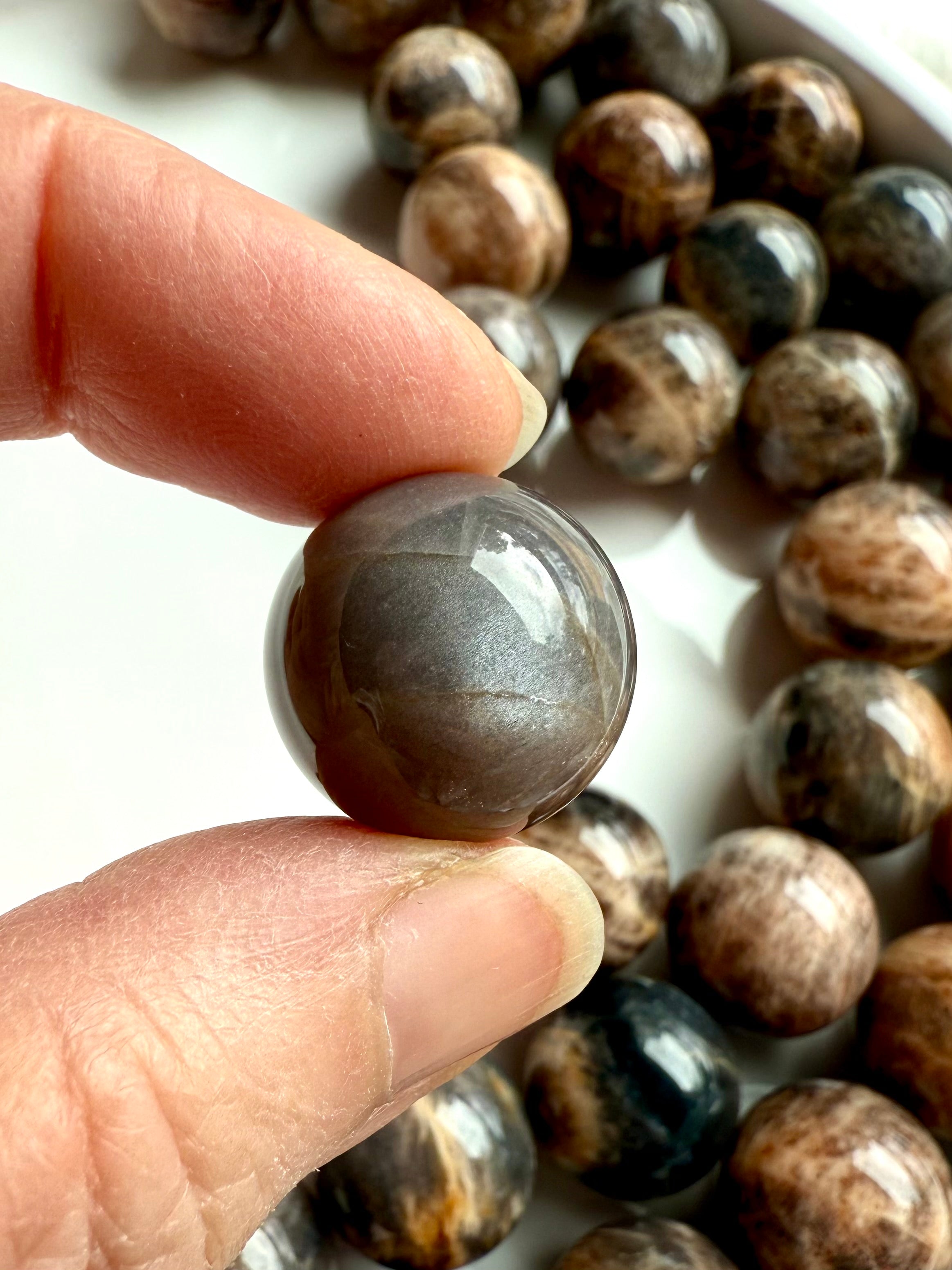 Closeup of a Black Moonstone sphere with dark, shimmery surface & chatoyancy for intuition, grounding, & emotional balance 
