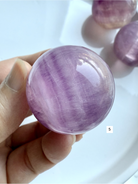 rare pink and purple Fluorite sphere with natural silky banding and polished glossy finish held in hand