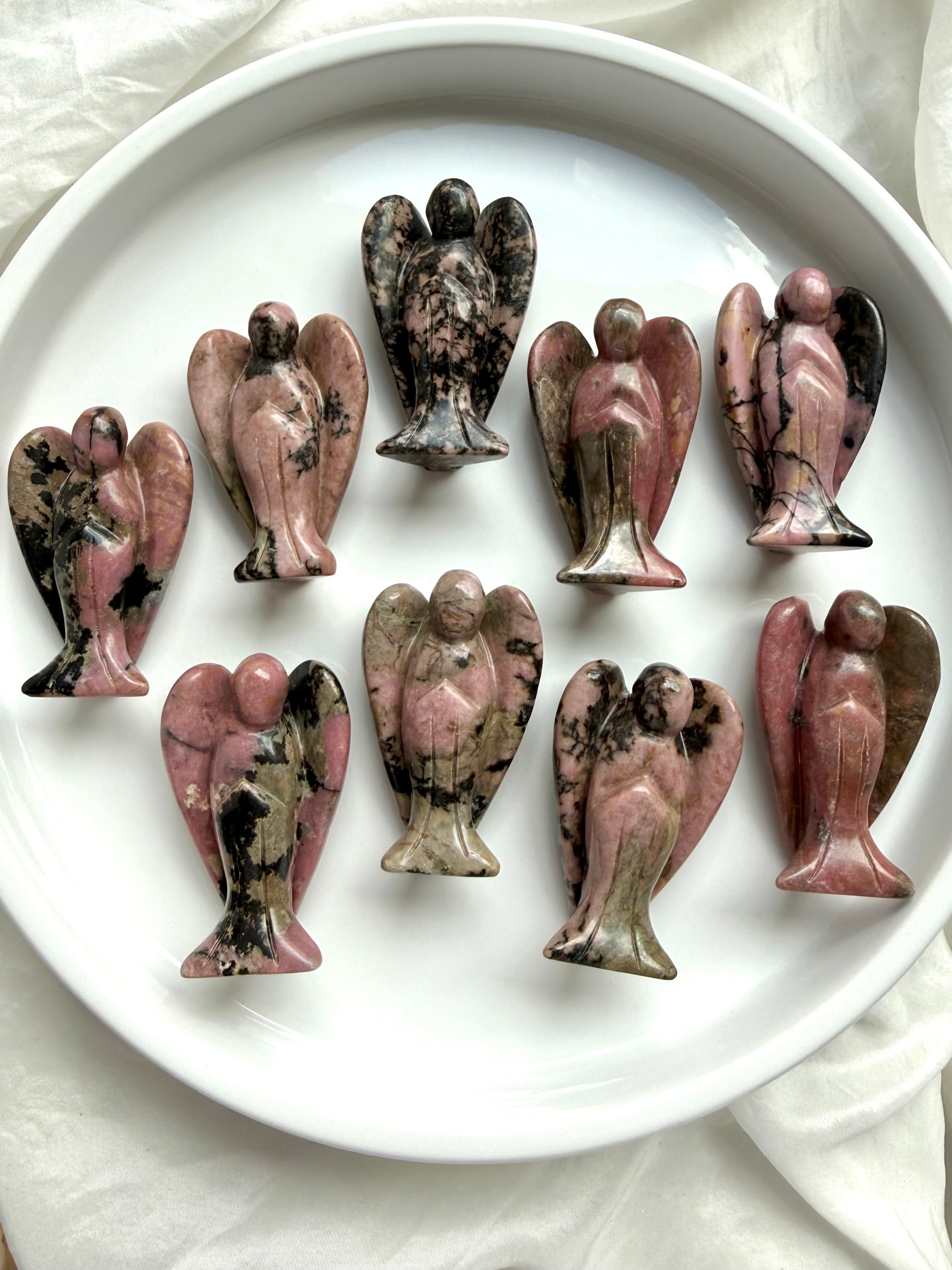 rhodonite angel carvings with pink and black natural patterns arranged on a white plate for heart healing and compassion