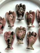 Collection of Rhodonite angel figurines with pink, black, and tan hues on a white surface
