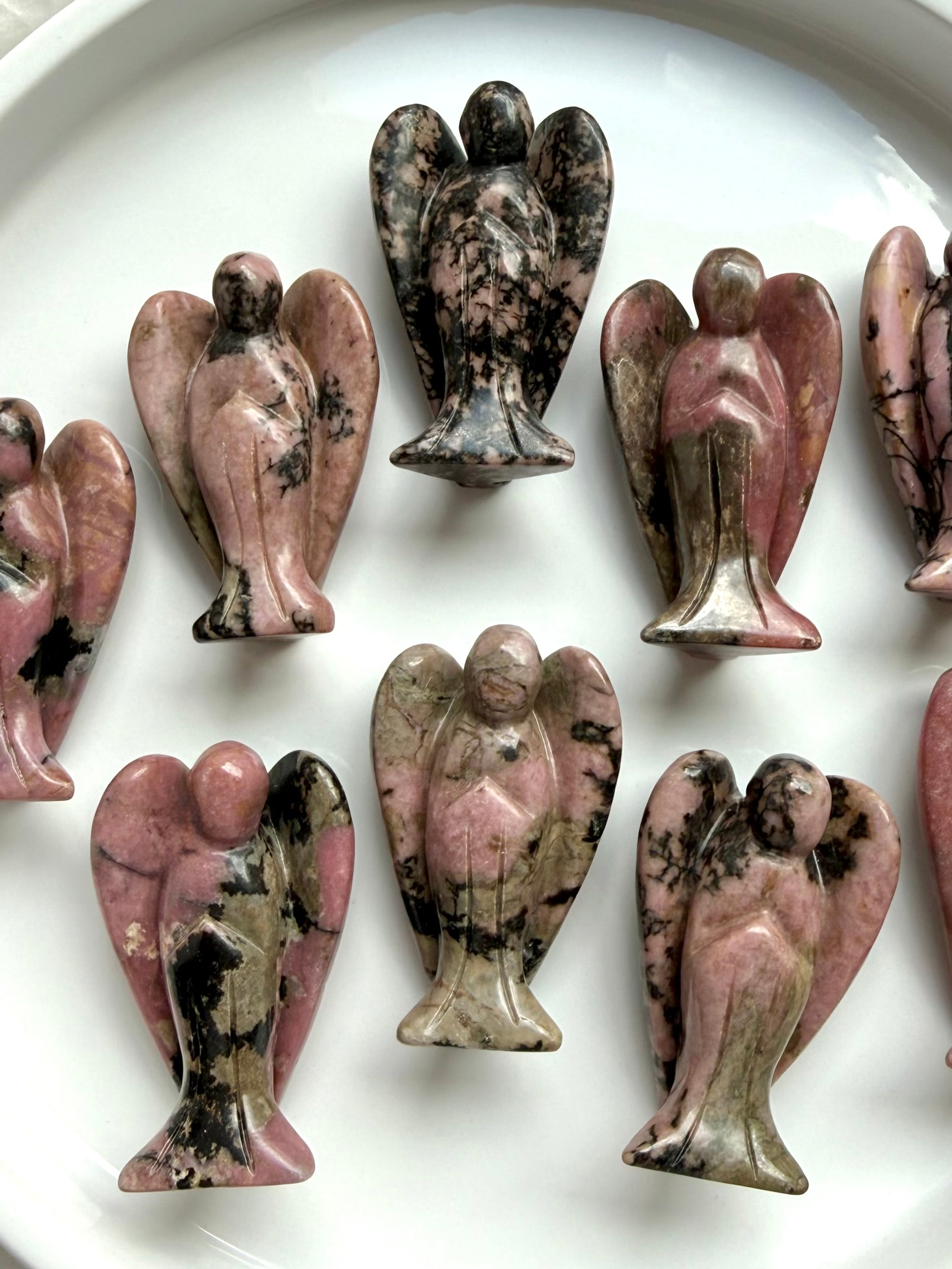 Collection of Rhodonite angel figurines with pink, black, and tan hues on a white surface