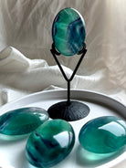 Large banded teal fluorite palm stone displayed on stand with oceanic blue green color and translucent depth