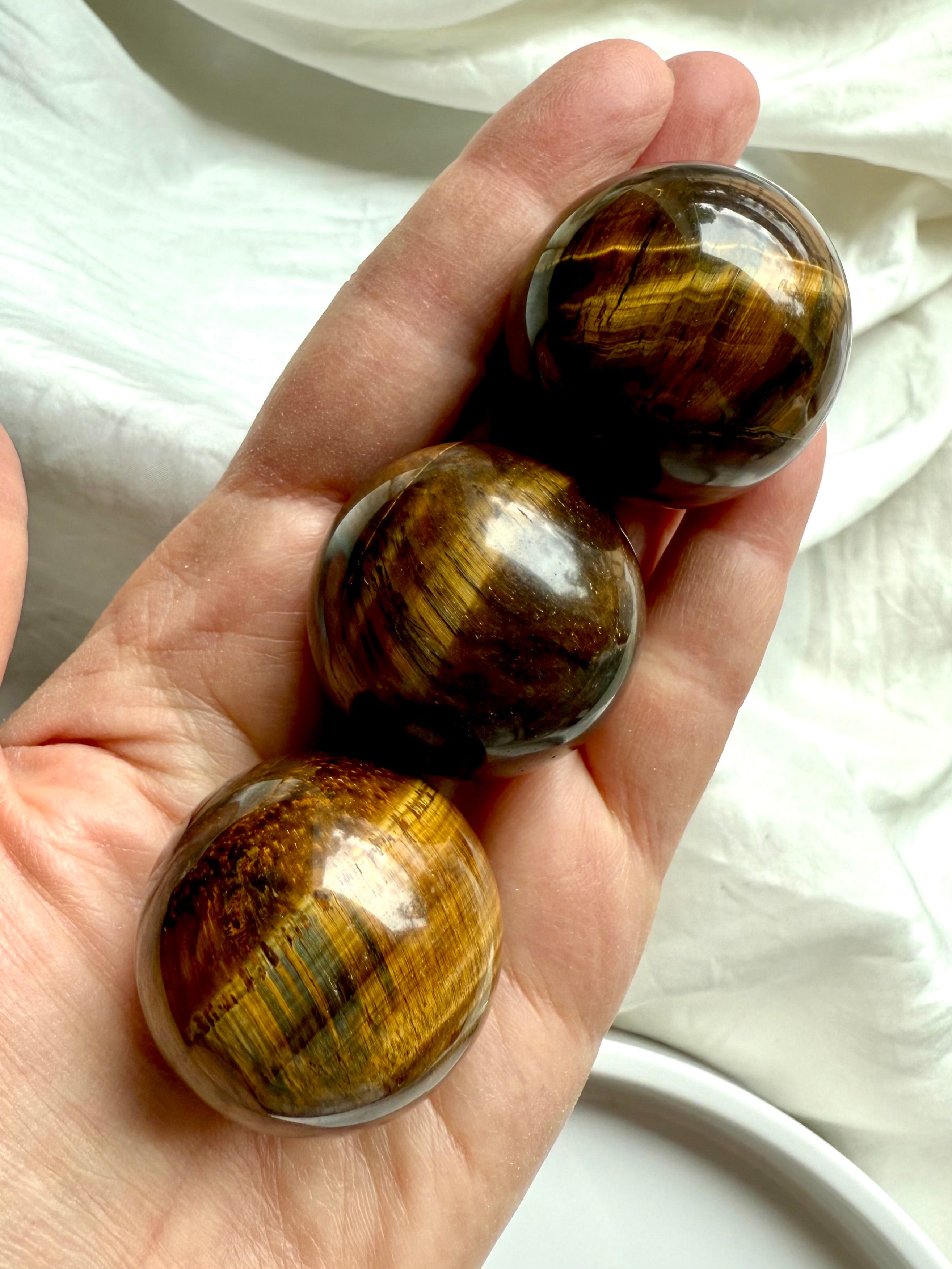 Three polished Tiger’s Eye spheres on a hand with golden brown shimmer — Root Chakra healing crystals