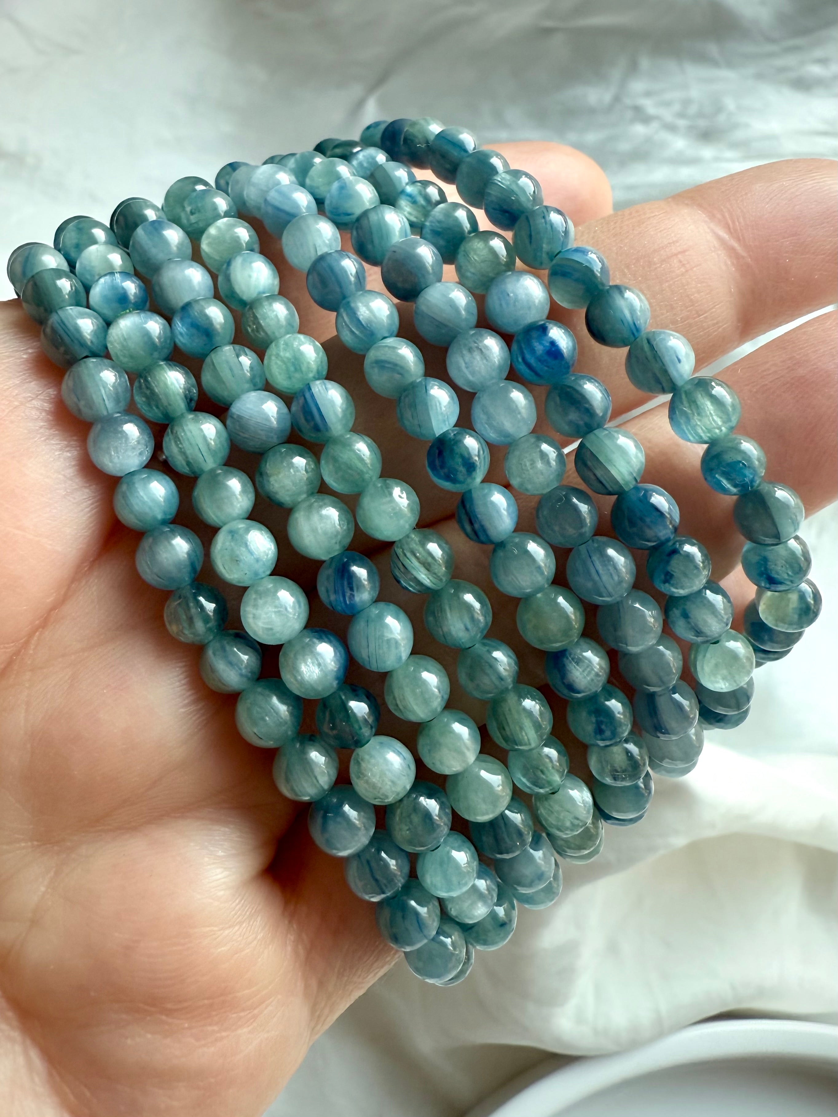 hand holding multiple blue-green kyanite crystal bracelets with radiant aqua, teal, and forest hues for intuition and spiritual clarity