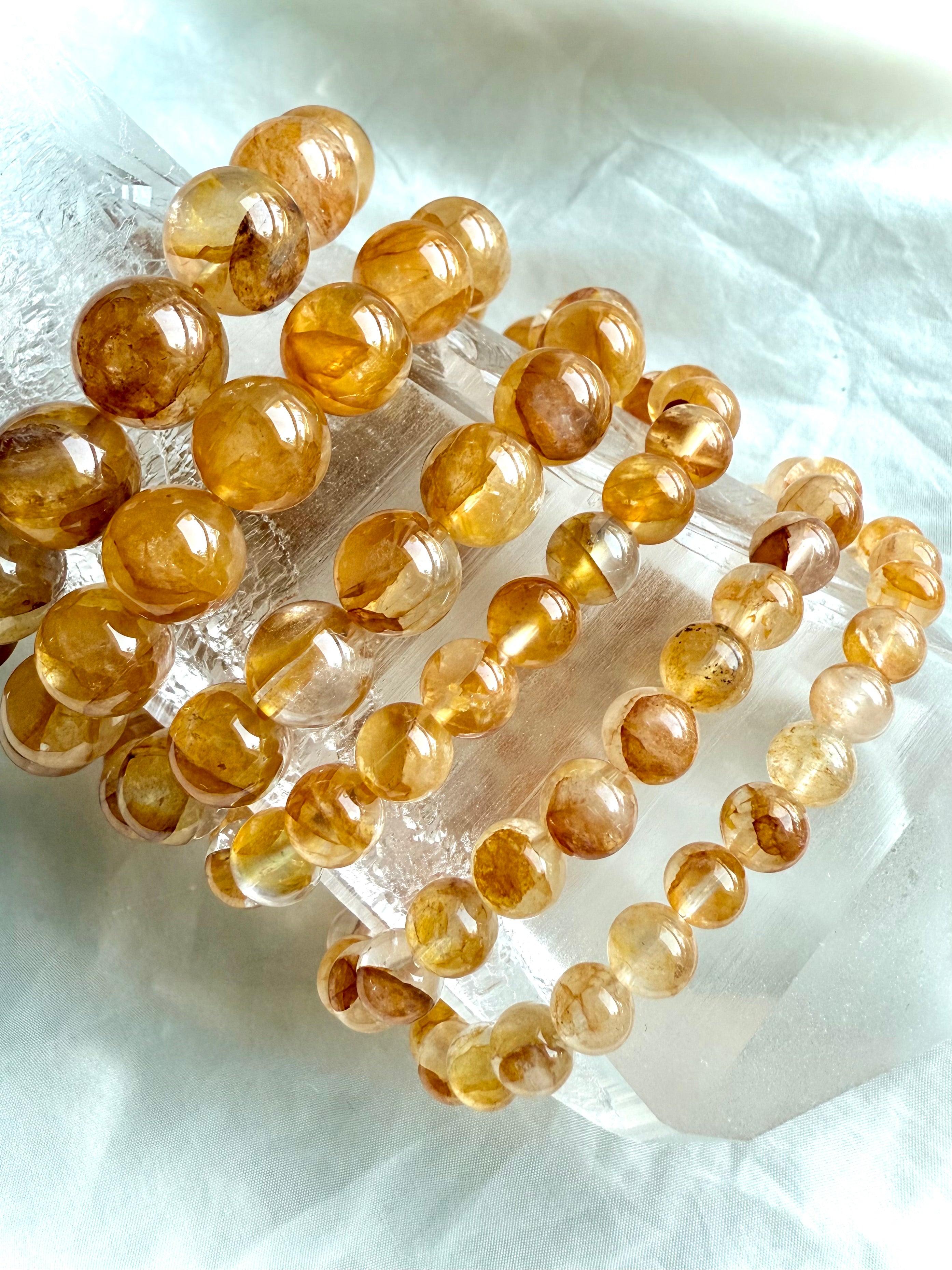 Golden Healer Quartz beaded bracelet stack on quartz point, highlighting radiant golden tones, transparency, and natural variation in bead sizes.