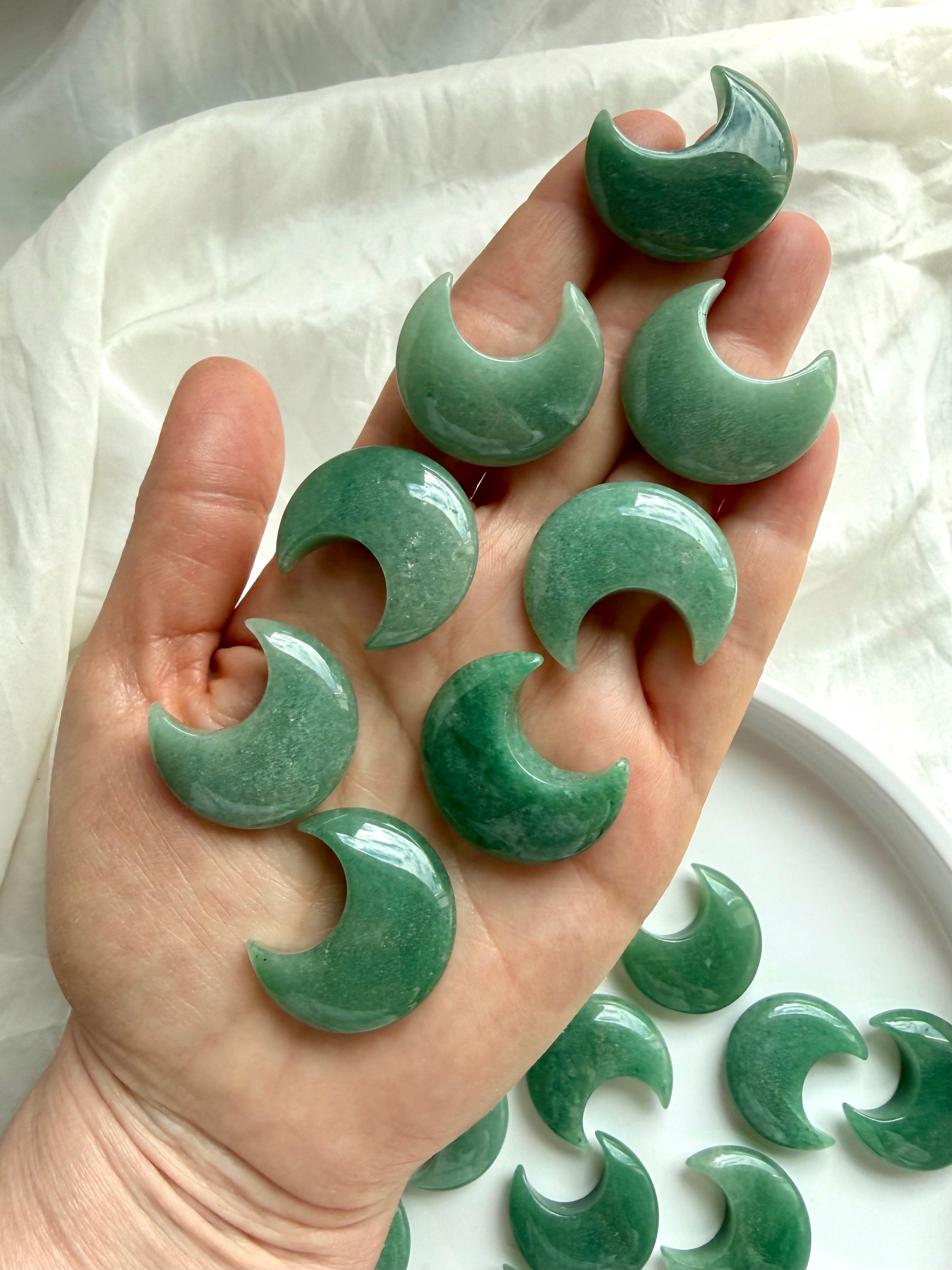 Green Aventurine crescent moons displayed on hand over white silk, Heart Chakra crystals for healing, peace, and grounding