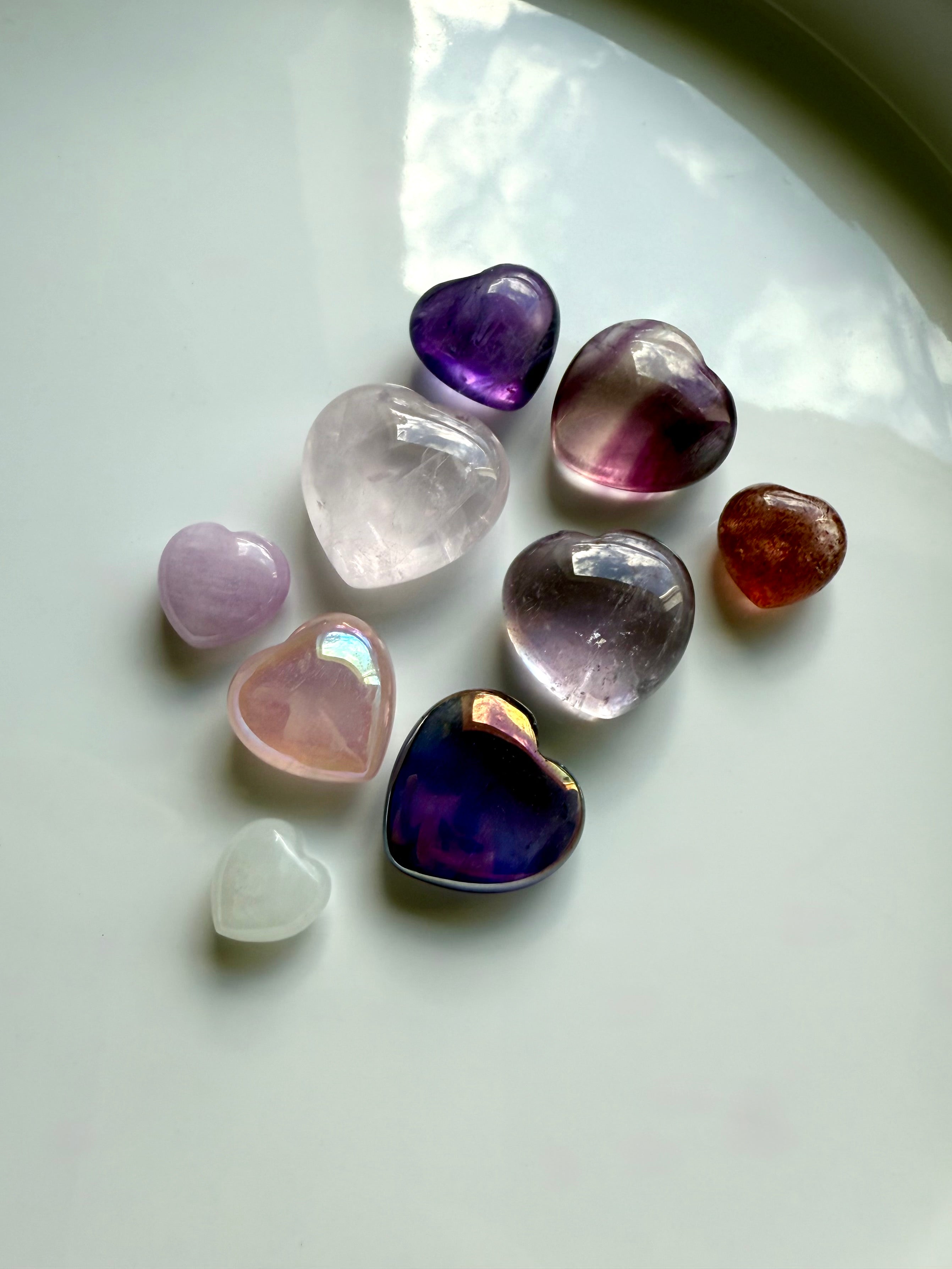 Wide view of pink and purple mini crystal hearts on white, highlighting color, aura coating, and polished finish.