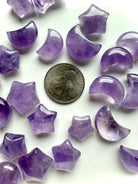 Close-up of amethyst star and crescent moon carvings shown with a US quarter for scale, highlighting smooth polish and translucence