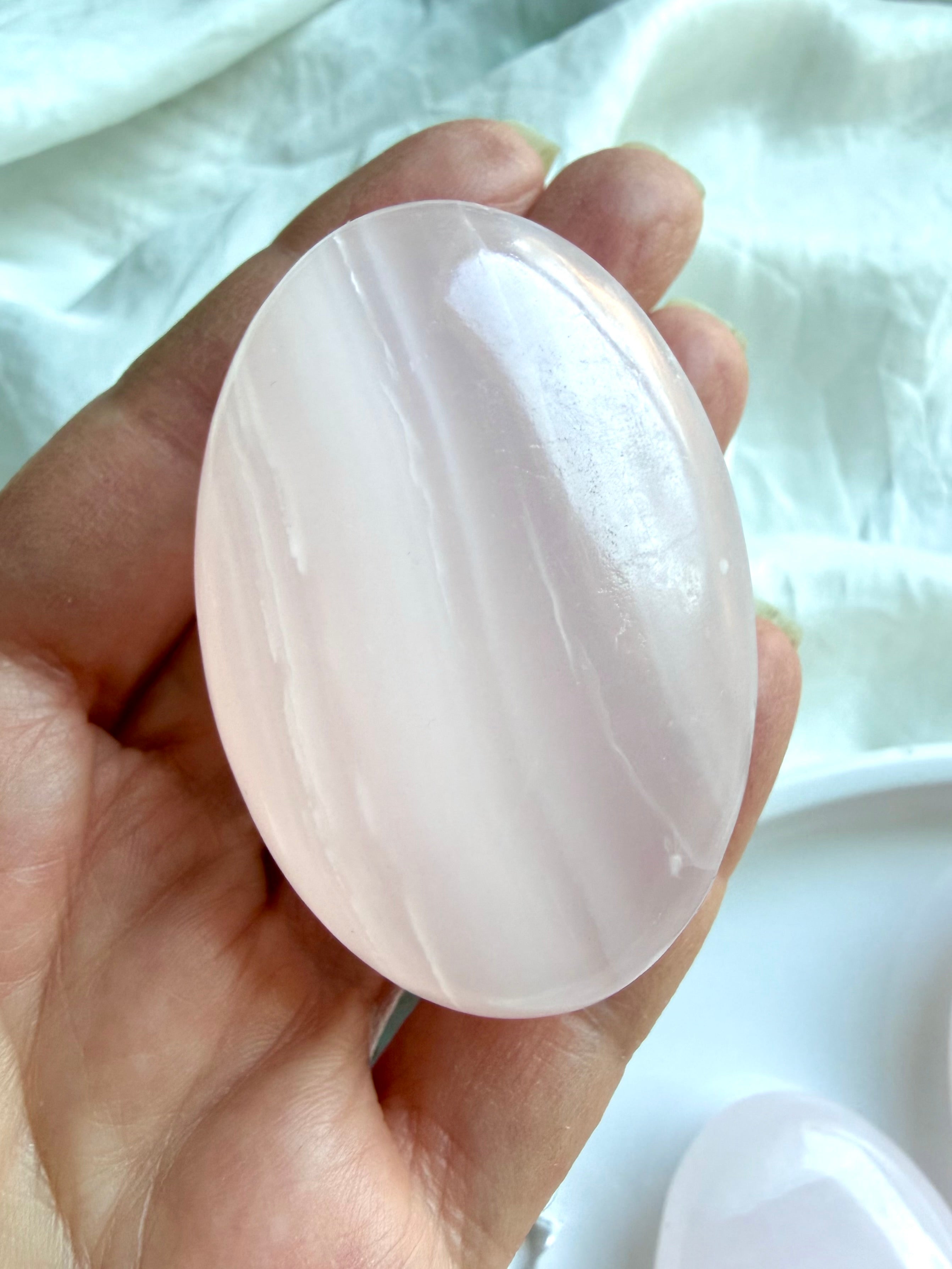 Pink Calcite palm stone held in hand with polished finish and gentle blush pink layers