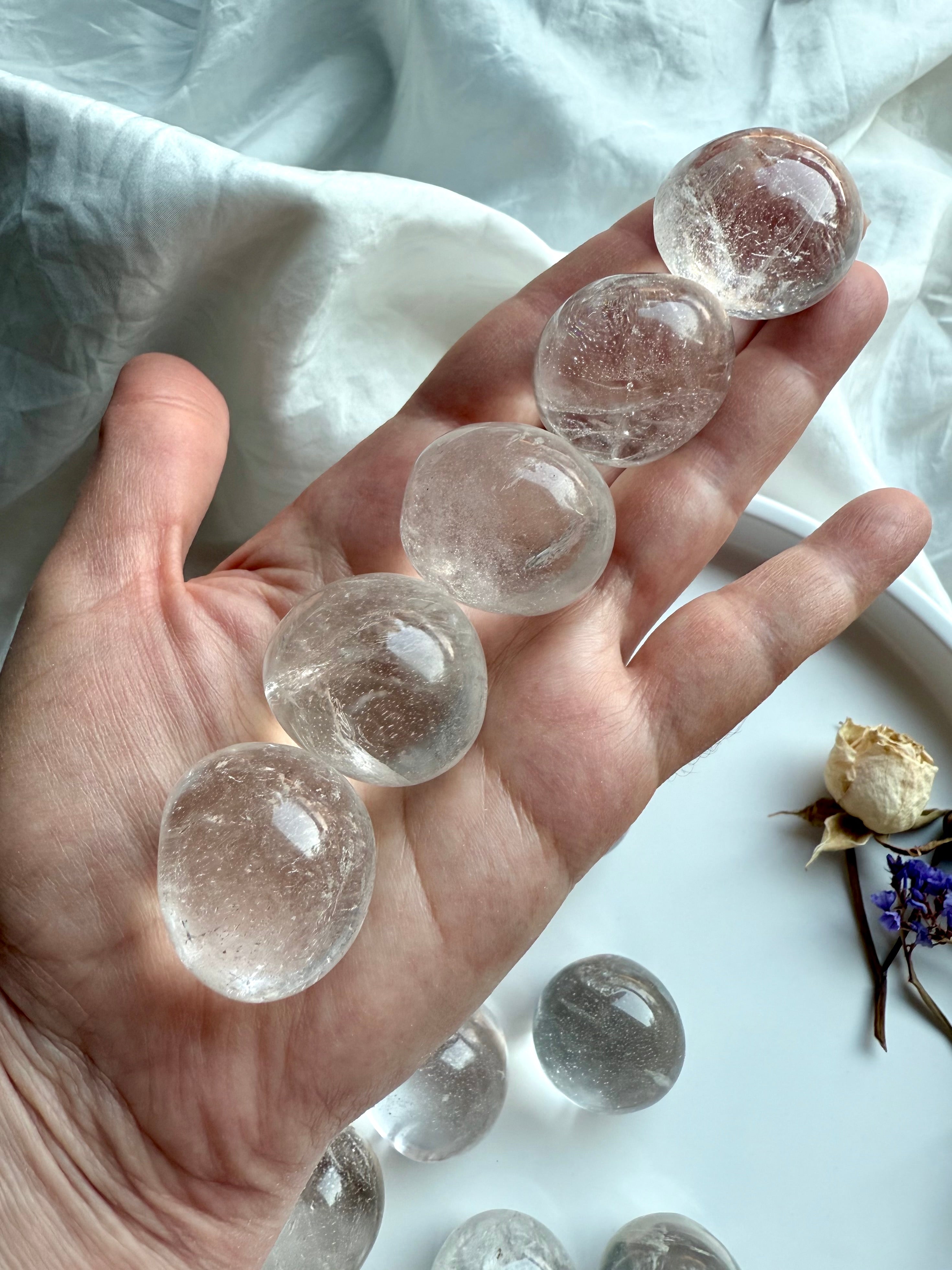 Row of Clear Quartz tumbled stones resting in hand to show size, shape, and natural inclusions